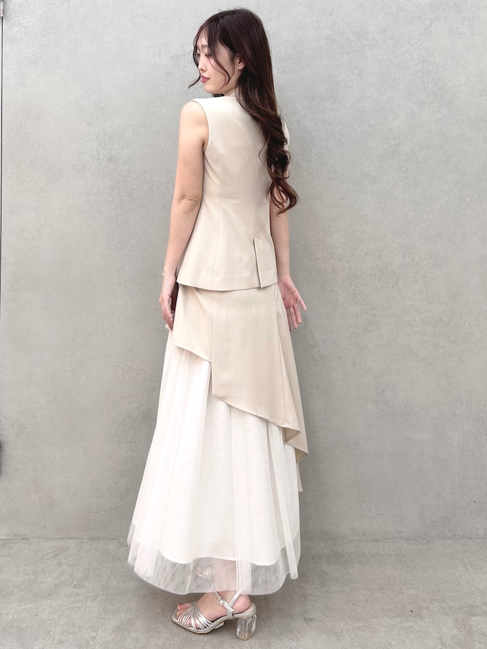 シルバー系のサンダル、ベージュ系のスカート、ベージュ系のベストを着用したレディースの春コーディネートの3枚目の写真