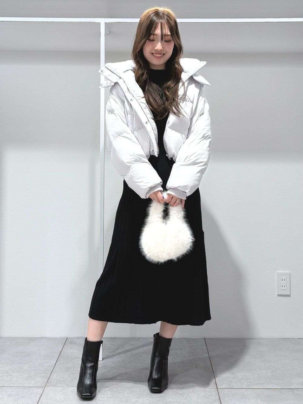 ブラック系のワンピース、ホワイト系のハンドバッグ、ブラック系のブーツを着用したレディースの秋コーディネートの2枚目の写真