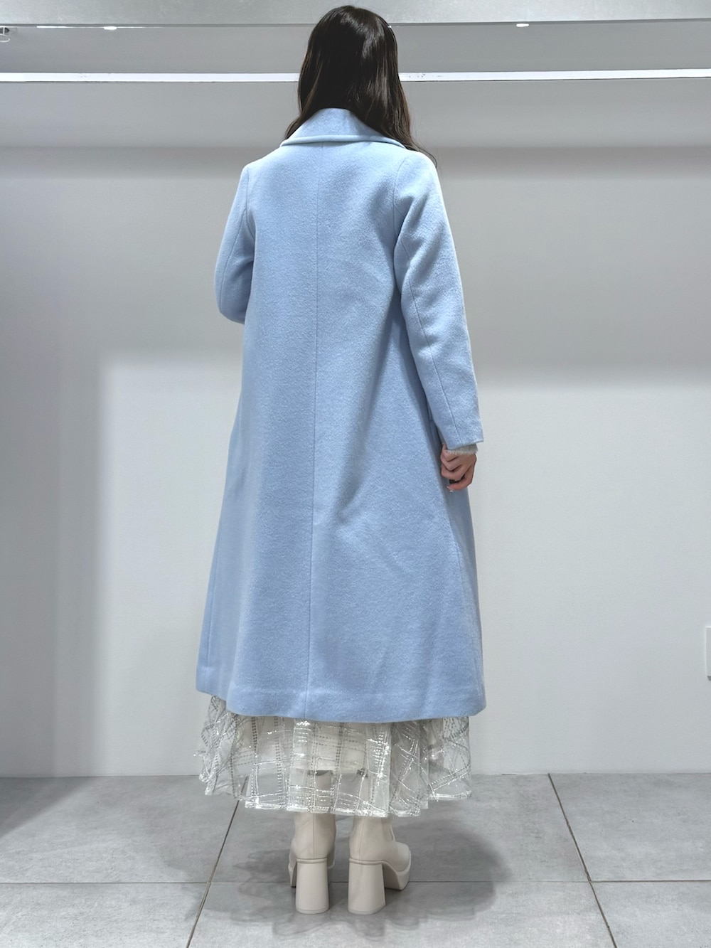 ブルー系のチェスターコート、ホワイト系のスカート、グレー系のカーディガン/ボレロを着用したレディースの秋コーディネートの4枚目の写真