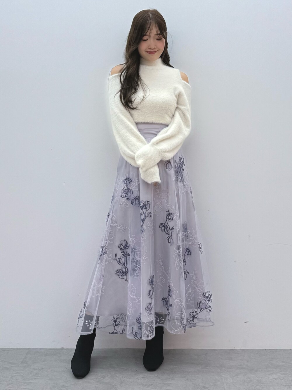 パープル系のスカート、ホワイト系のニット/セーター、ブラック系のブーツを着用したレディースの秋コーディネートの2枚目の写真