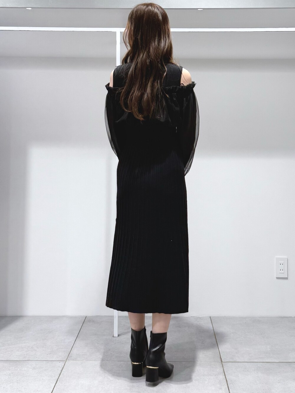 ホワイト系のハンドバッグ、ブラック系のワンピース、ブラック系のブーツを着用したレディースの秋コーディネートの4枚目の写真