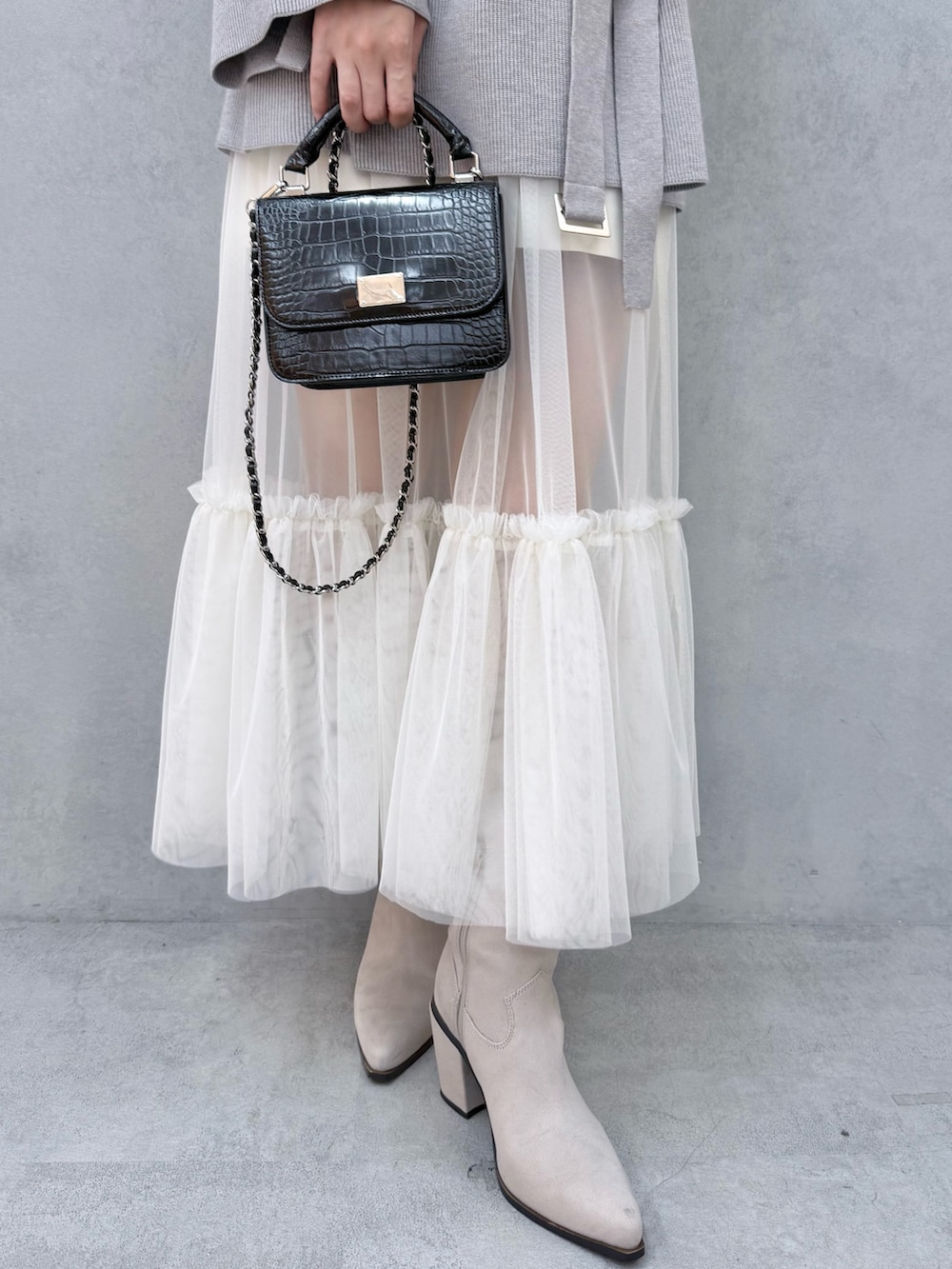 ブラック系のハンドバッグ、グレー系のニット/セーター、ホワイト系のスカートを着用したレディースの夏コーディネートの6枚目の写真