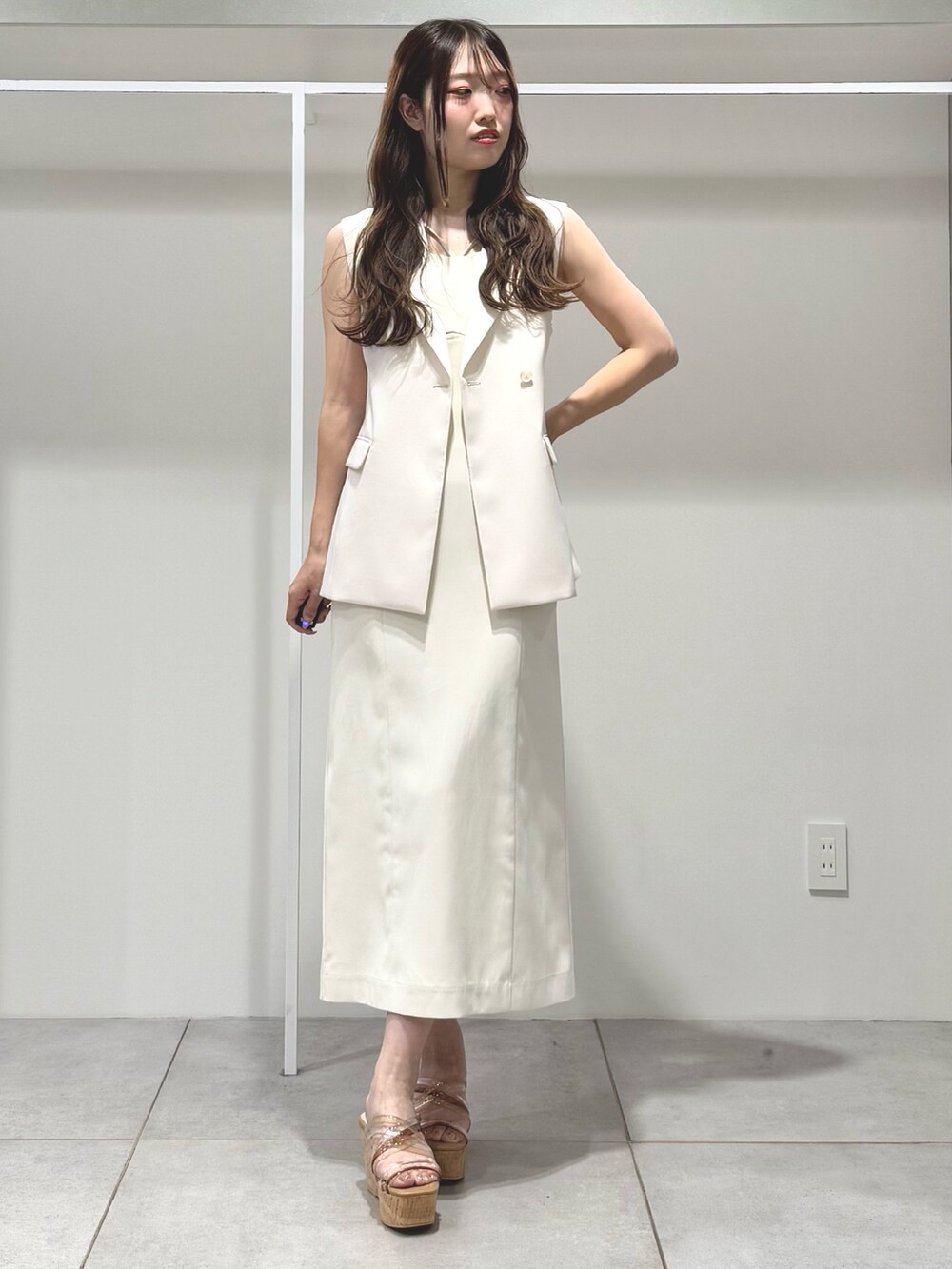 ホワイト系のワンピース、ベージュ系のサンダル、ホワイト系のベストを着用したレディースの春コーディネートの2枚目の写真