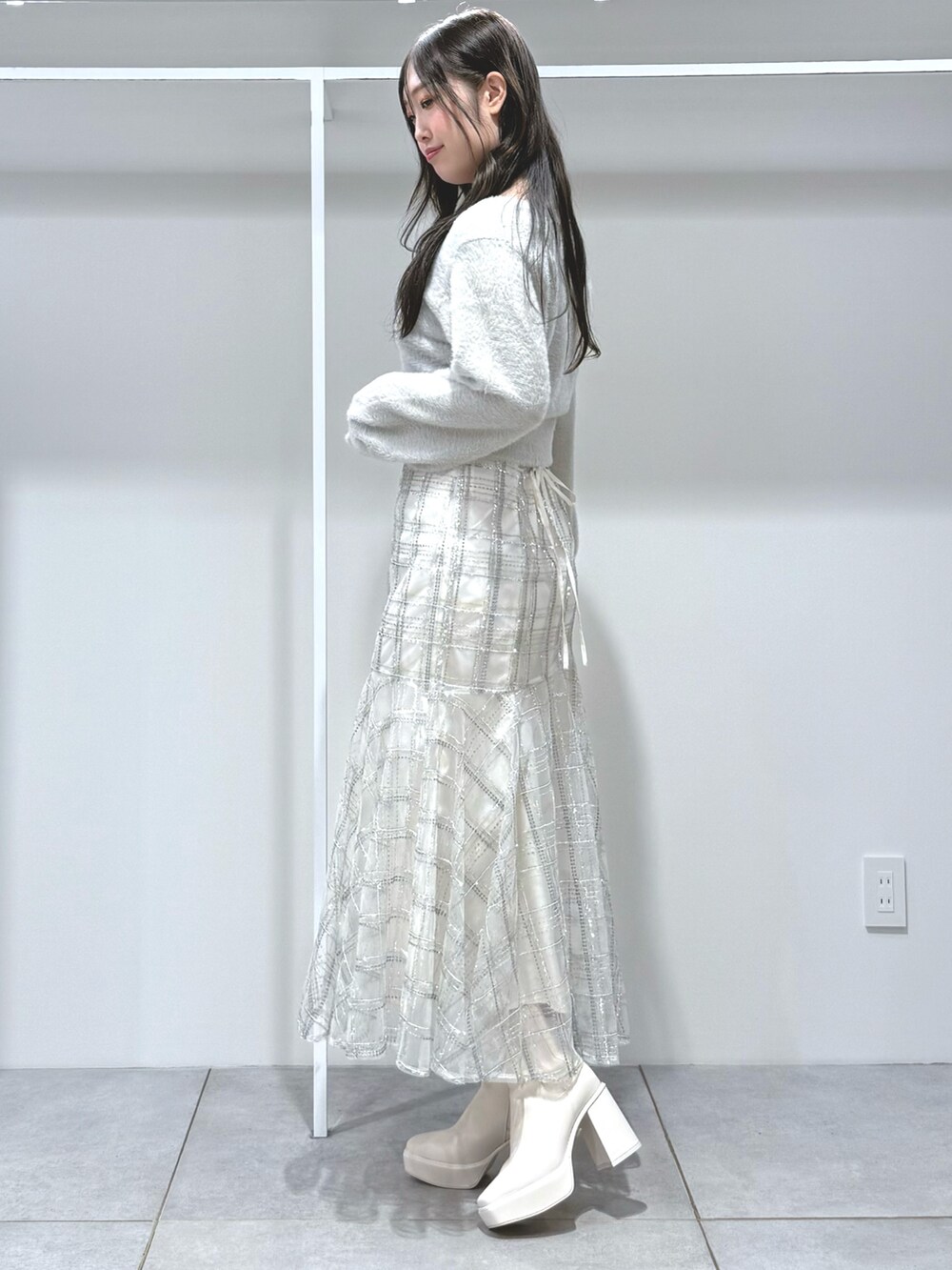 グレー系のカーディガン/ボレロ、ホワイト系のスカート、ホワイト系のブーツを着用したレディースの秋コーディネートの2枚目の写真