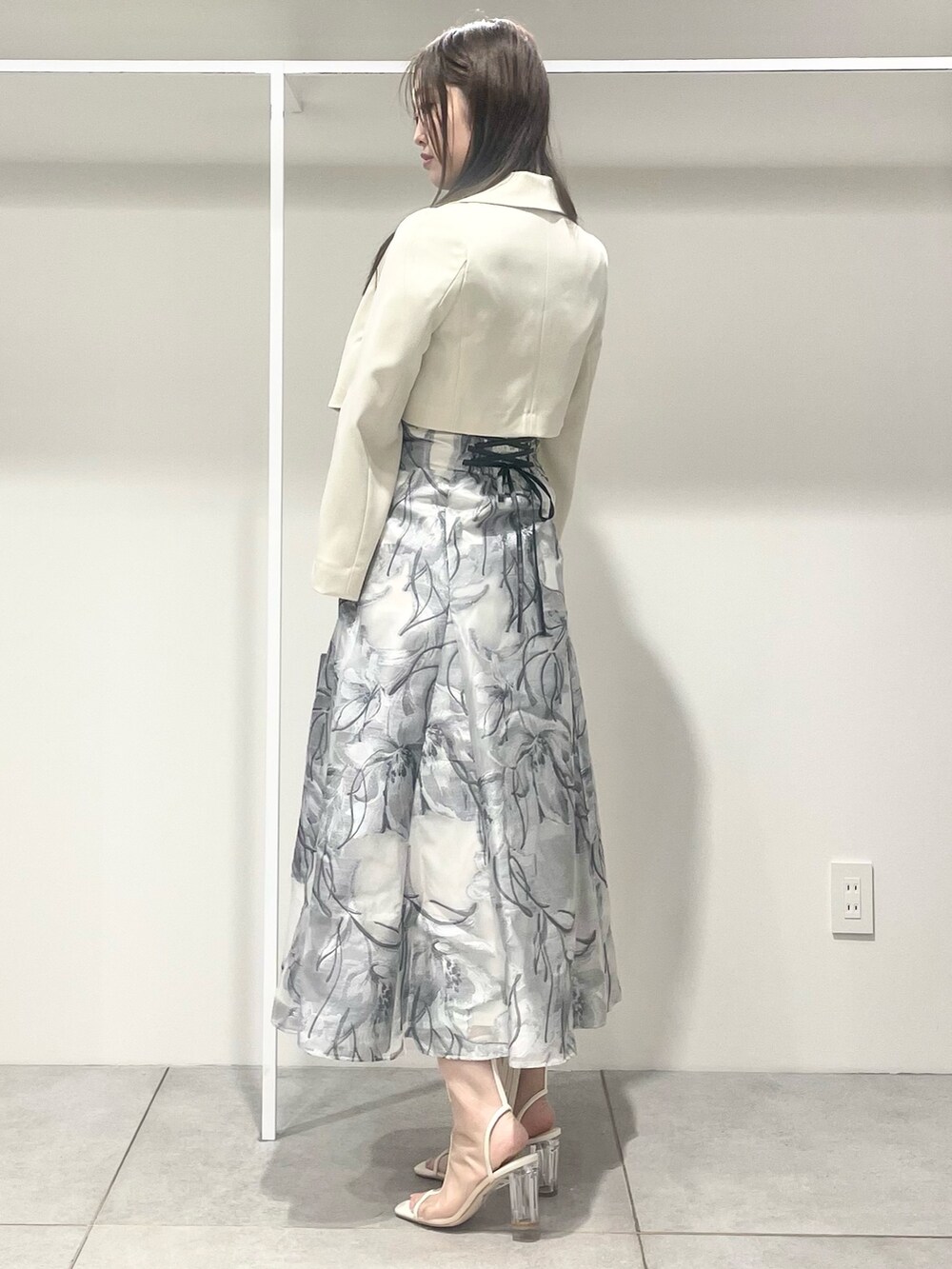 シルバー系のハンドバッグ、ホワイト系のテーラードジャケット、ブルー系のニット/セーターを着用したレディースの春コーディネートの2枚目の写真