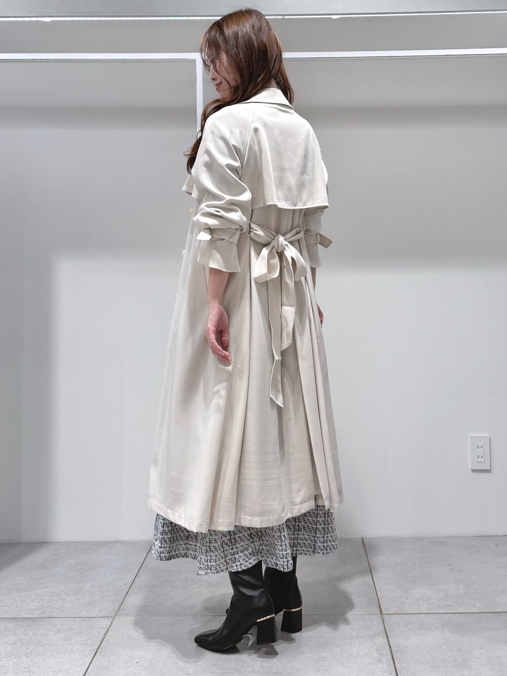 ホワイト系のトレンチコート、ブラック系のワンピース、ブラック系のブーツを着用したレディースの冬コーディネートの3枚目の写真