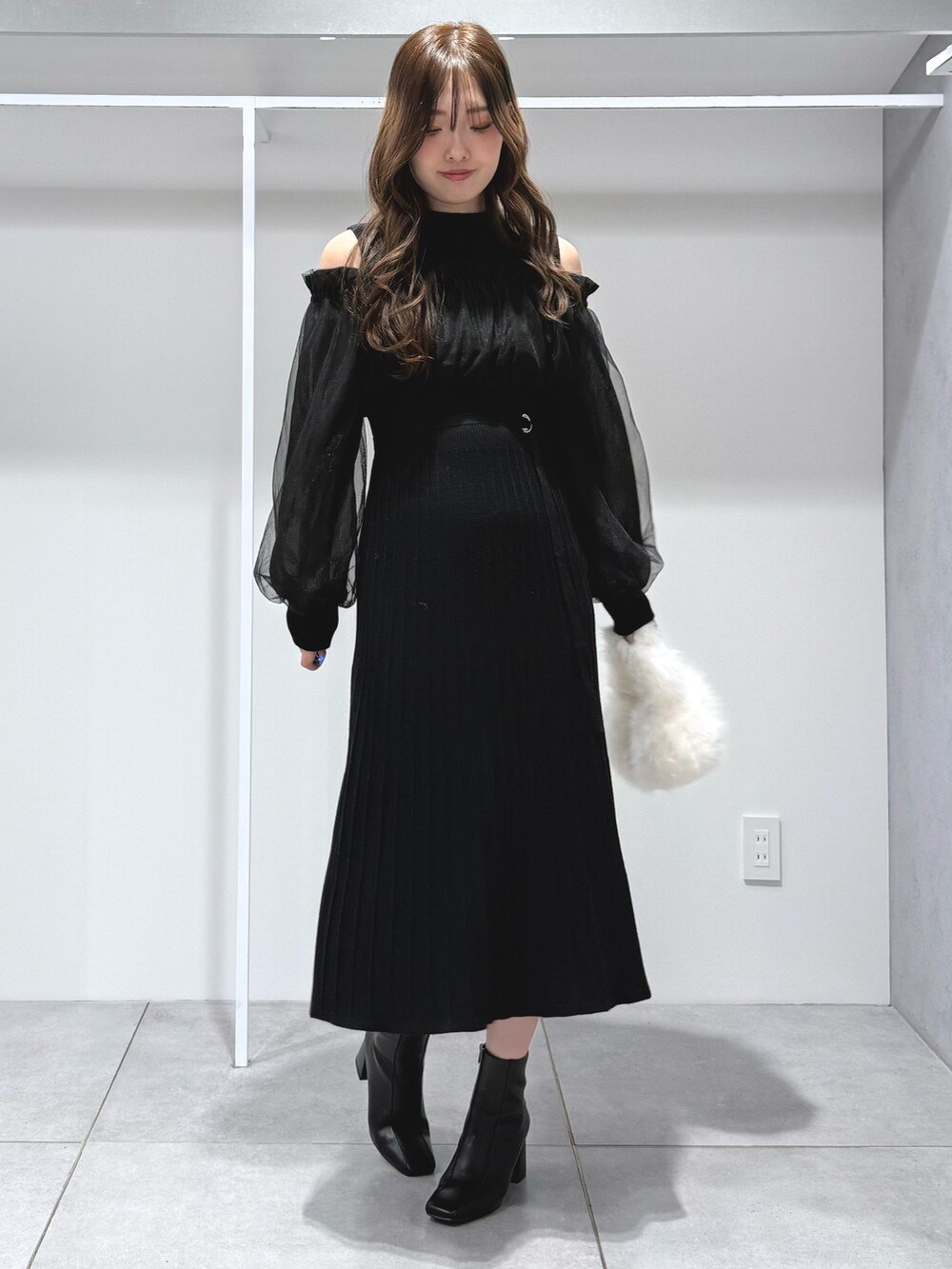 ホワイト系のハンドバッグ、ブラック系のワンピース、ブラック系のブーツを着用したレディースの秋コーディネートの2枚目の写真