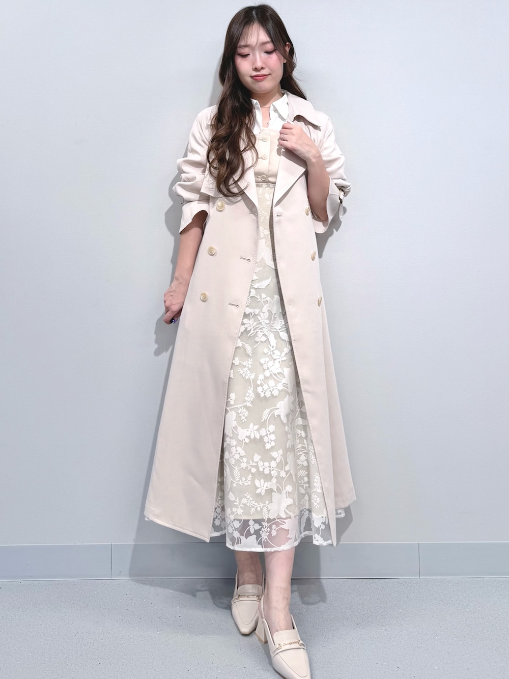 ベージュ系のワンピース、ホワイト系のパンプス、ホワイト系のトレンチコートを着用したレディースの冬コーディネートの2枚目の写真