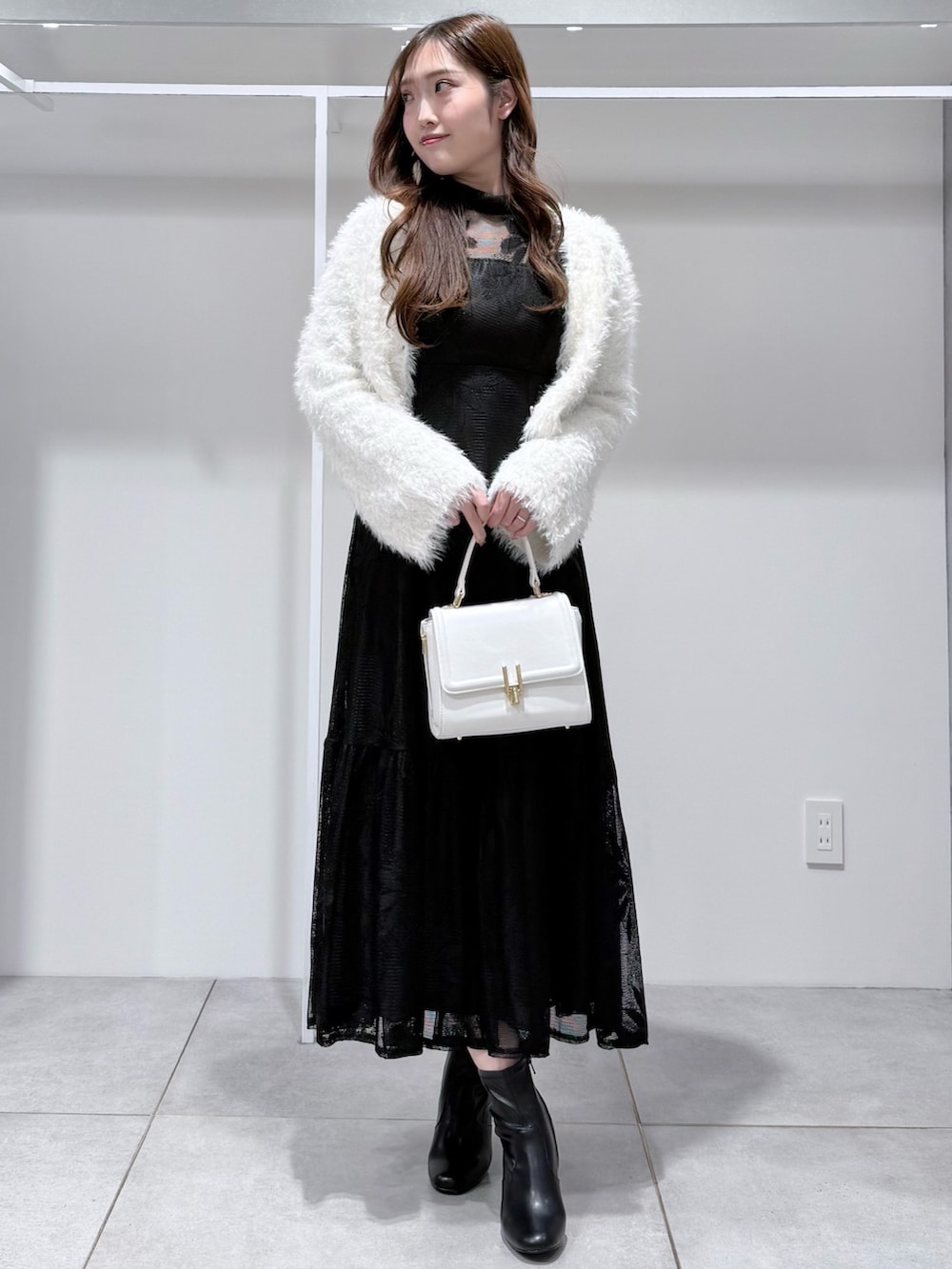 ブラック系のワンピース、ホワイト系のカーディガン/ボレロ、ホワイト系のハンドバッグを着用したレディースの冬コーディネートの2枚目の写真