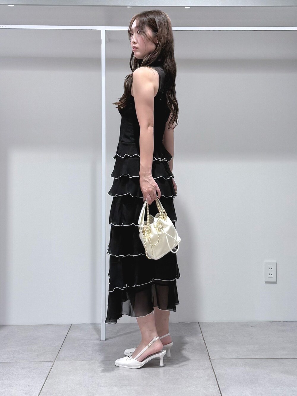 ホワイト系のハンドバッグ、ブラック系のワンピース、ホワイト系のパンプスを着用したレディースの夏コーディネートの3枚目の写真