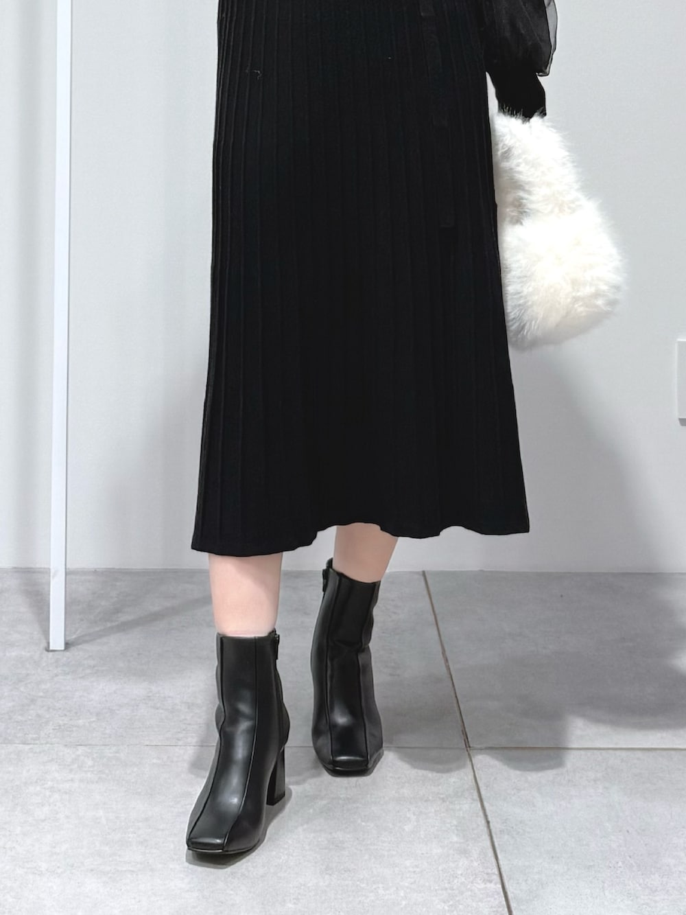 ホワイト系のハンドバッグ、ブラック系のワンピース、ブラック系のブーツを着用したレディースの秋コーディネートの7枚目の写真