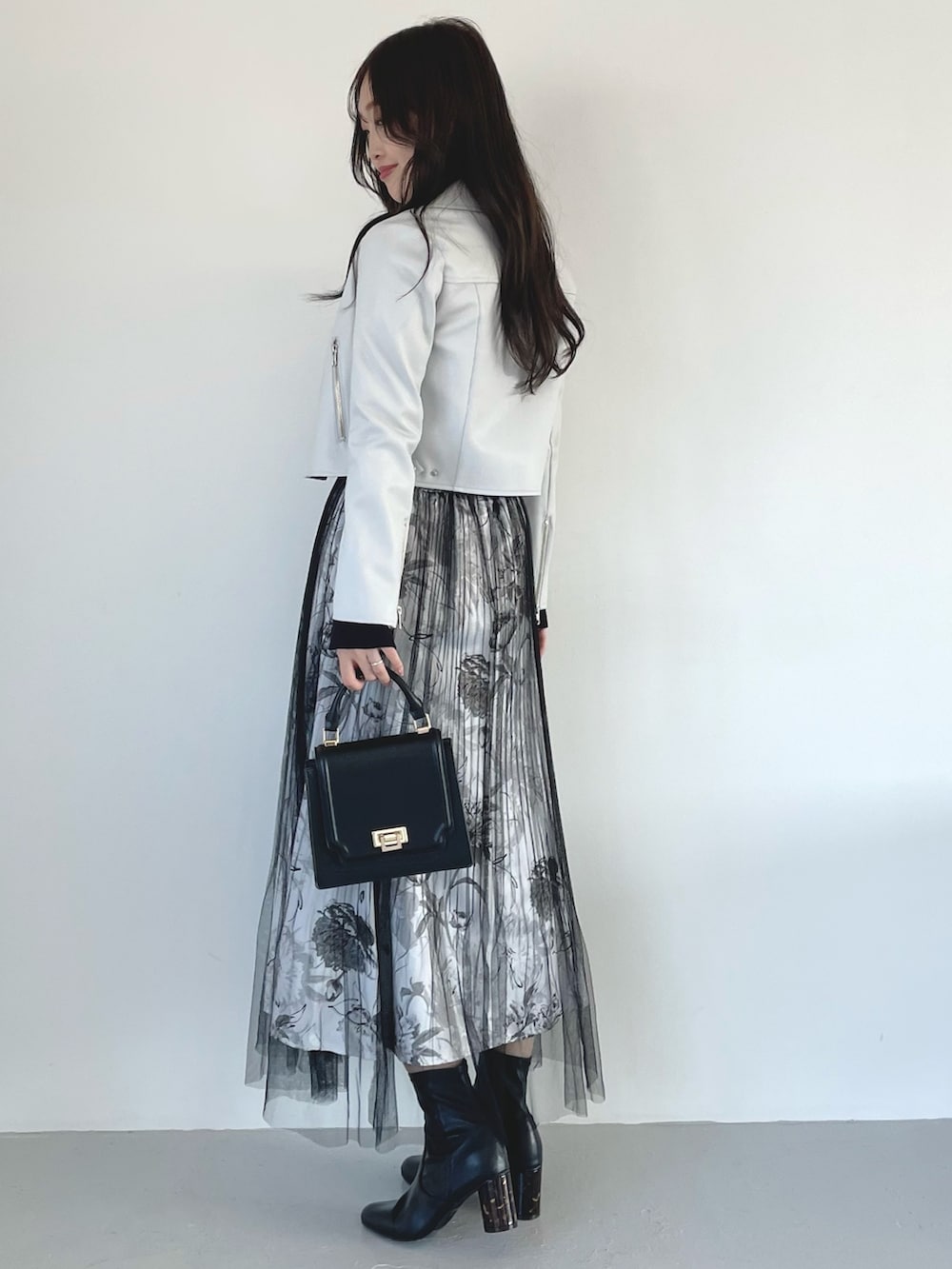 ブラック系のブーツ、ブラック系のスカート、ブラック系のハンドバッグを着用したレディースの春コーディネートの2枚目の写真