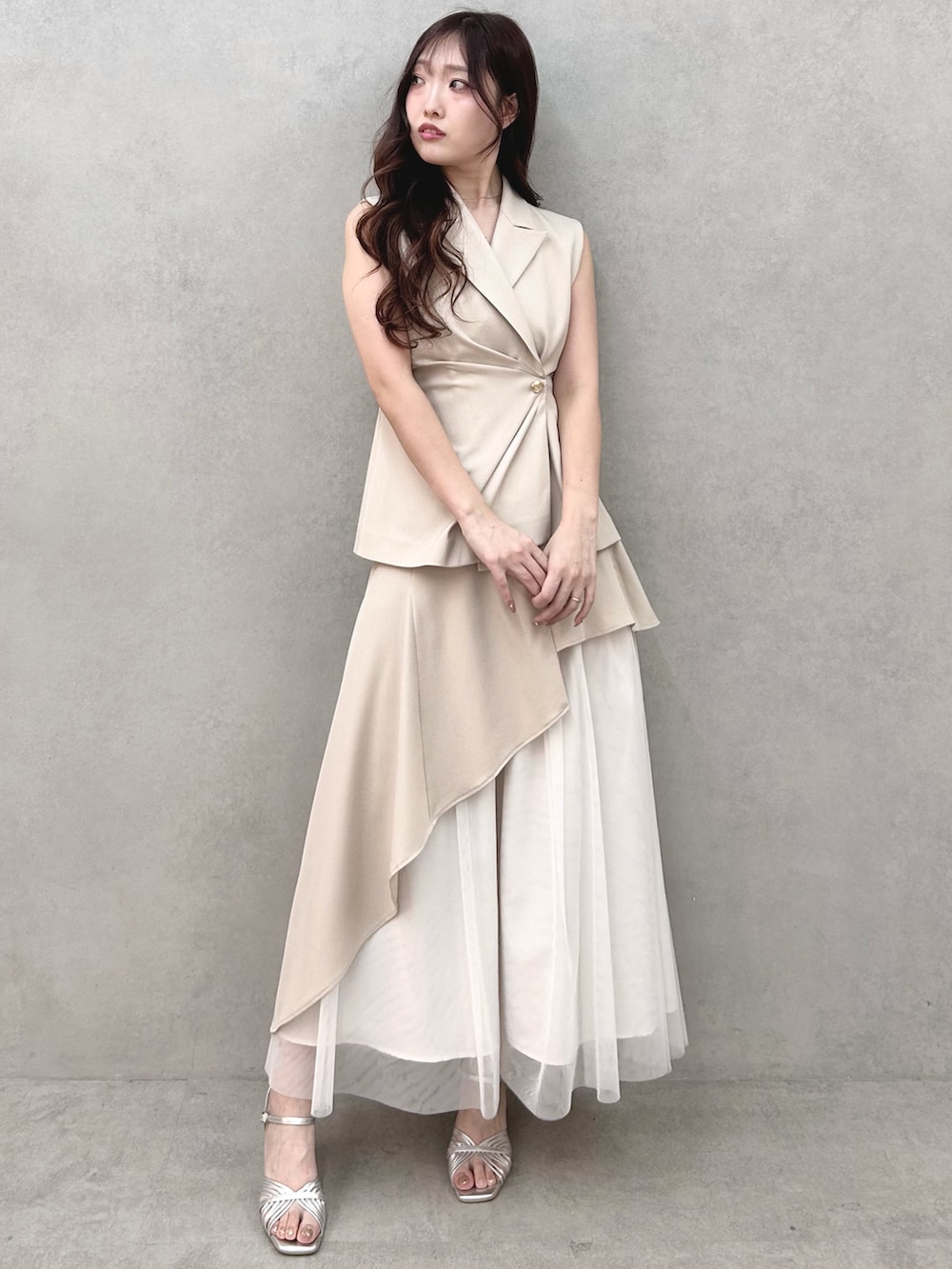 シルバー系のサンダル、ベージュ系のスカート、ベージュ系のベストを着用したレディースの春コーディネートの2枚目の写真