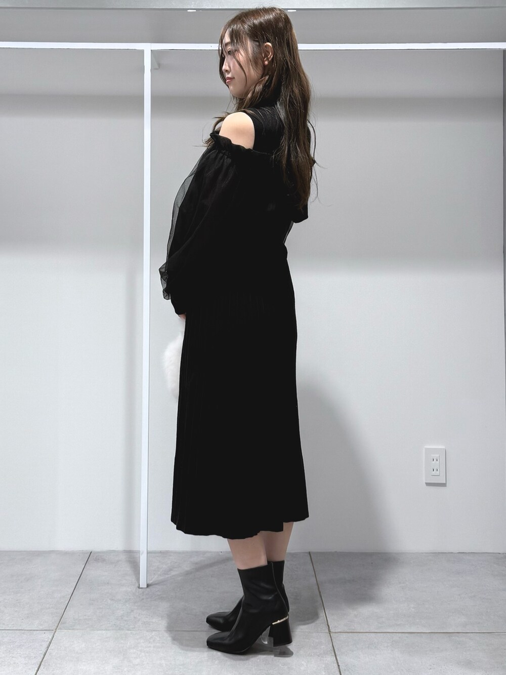 ホワイト系のハンドバッグ、ブラック系のワンピース、ブラック系のブーツを着用したレディースの秋コーディネートの3枚目の写真