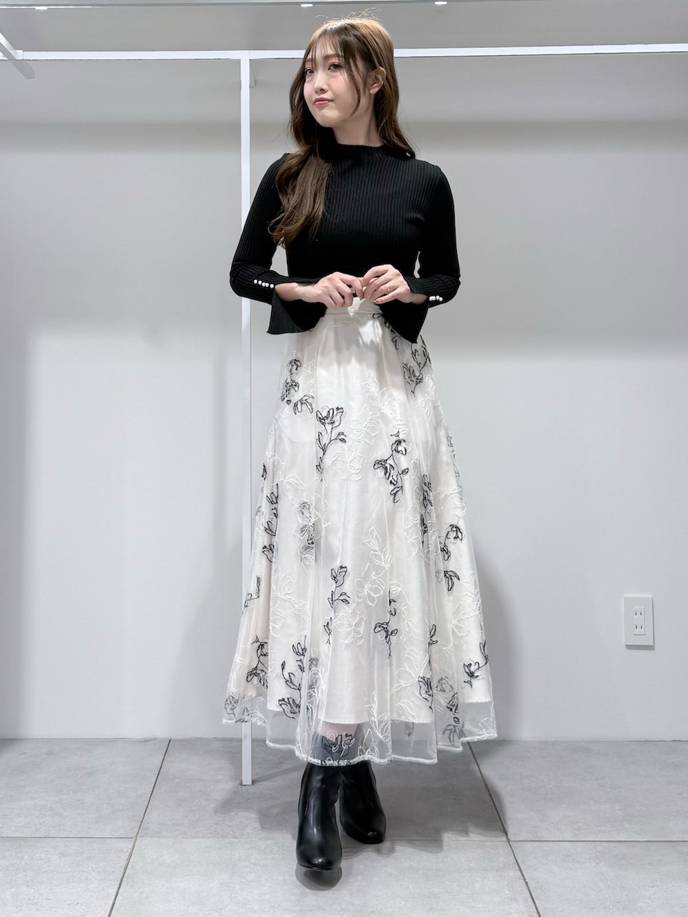 ブラック系のニット/セーター、ホワイト系のスカート、ブラック系のブーツを着用したレディースの冬コーディネートの2枚目の写真