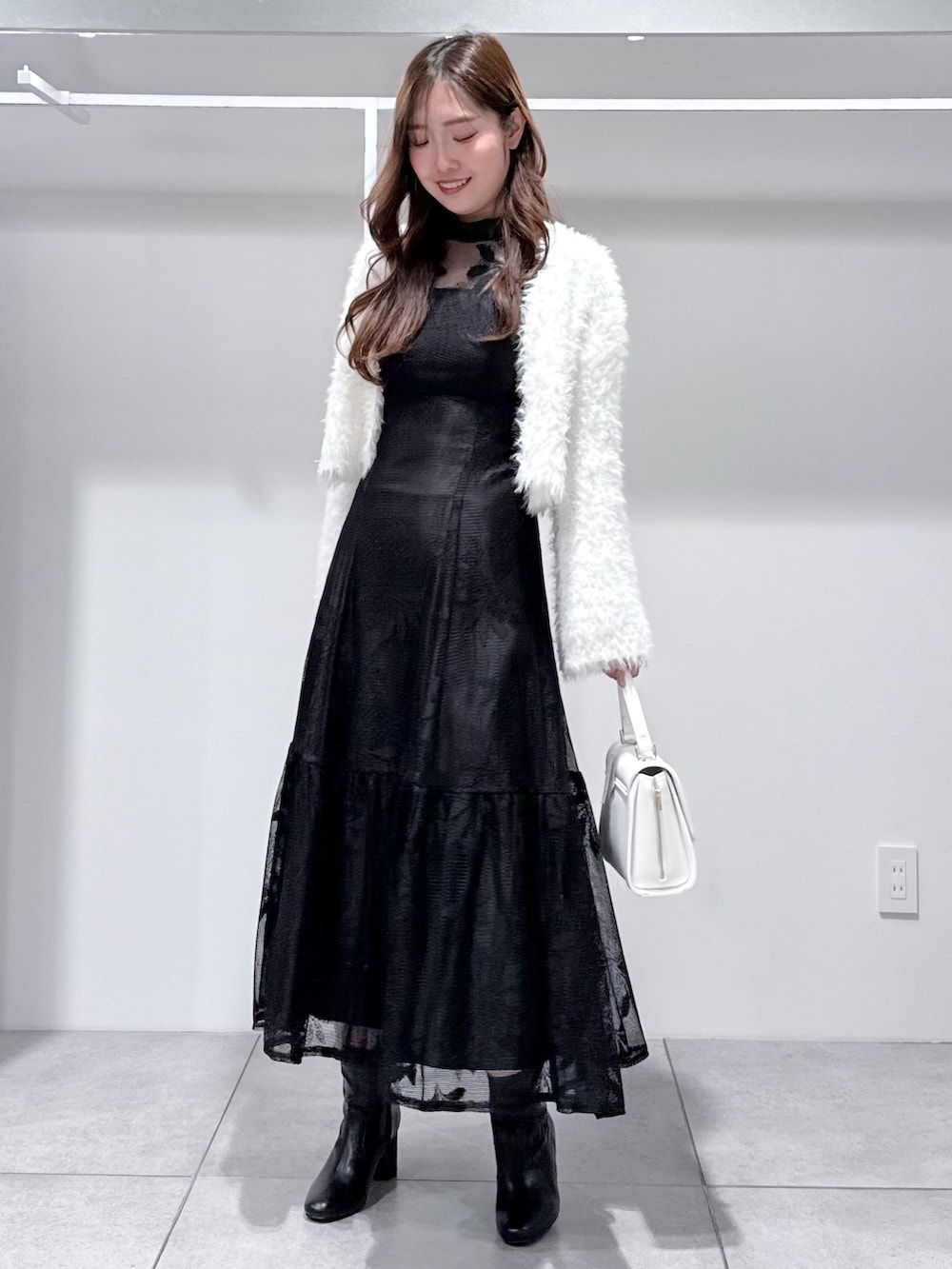 ブラック系のワンピース、ホワイト系のカーディガン/ボレロ、ホワイト系のハンドバッグを着用したレディースの冬コーディネートの3枚目の写真
