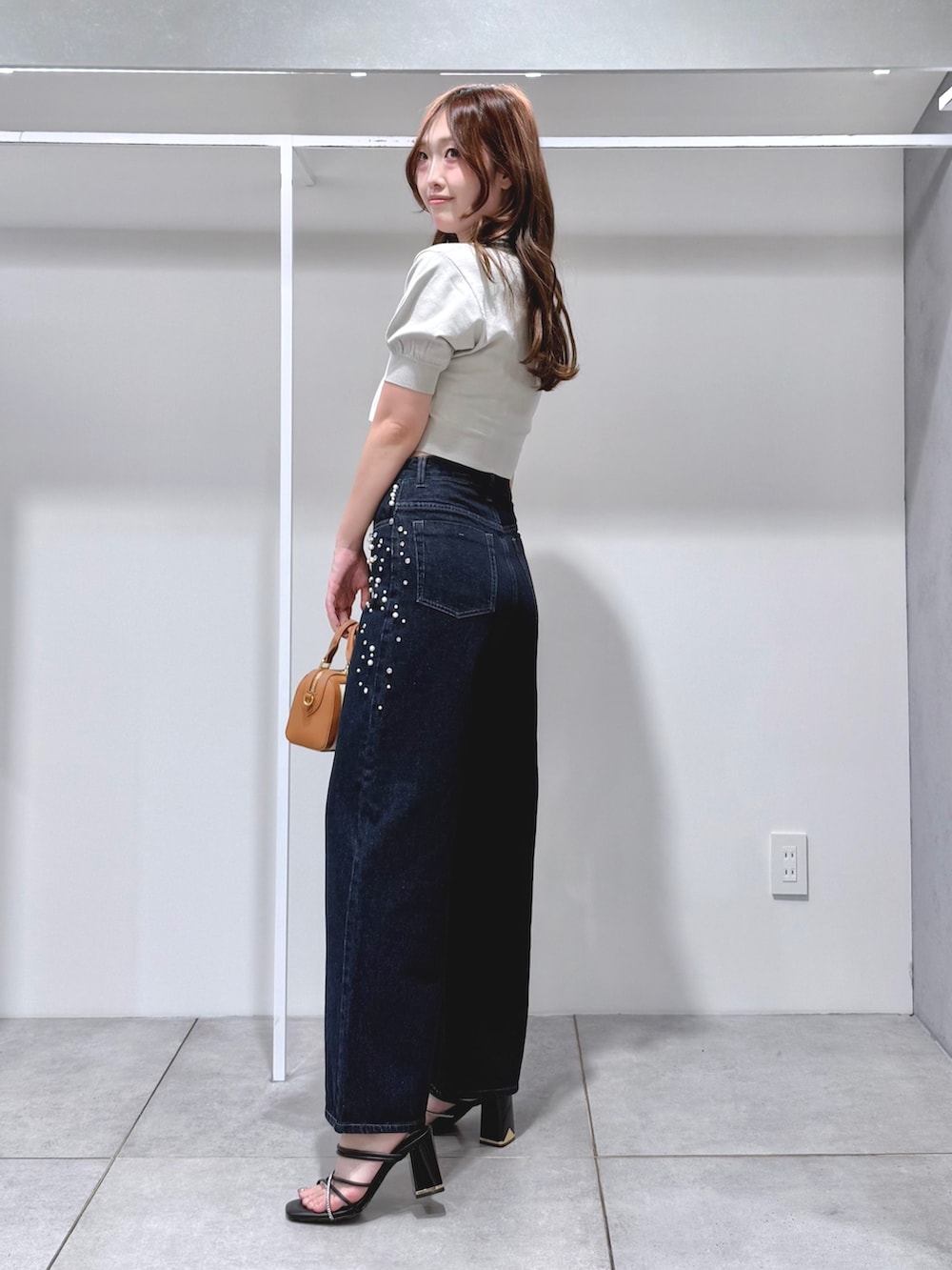 グリーン系のニット/セーター、ブルー系のデニムパンツ、ブラウン系のハンドバッグを着用したレディースの夏コーディネートの2枚目の写真