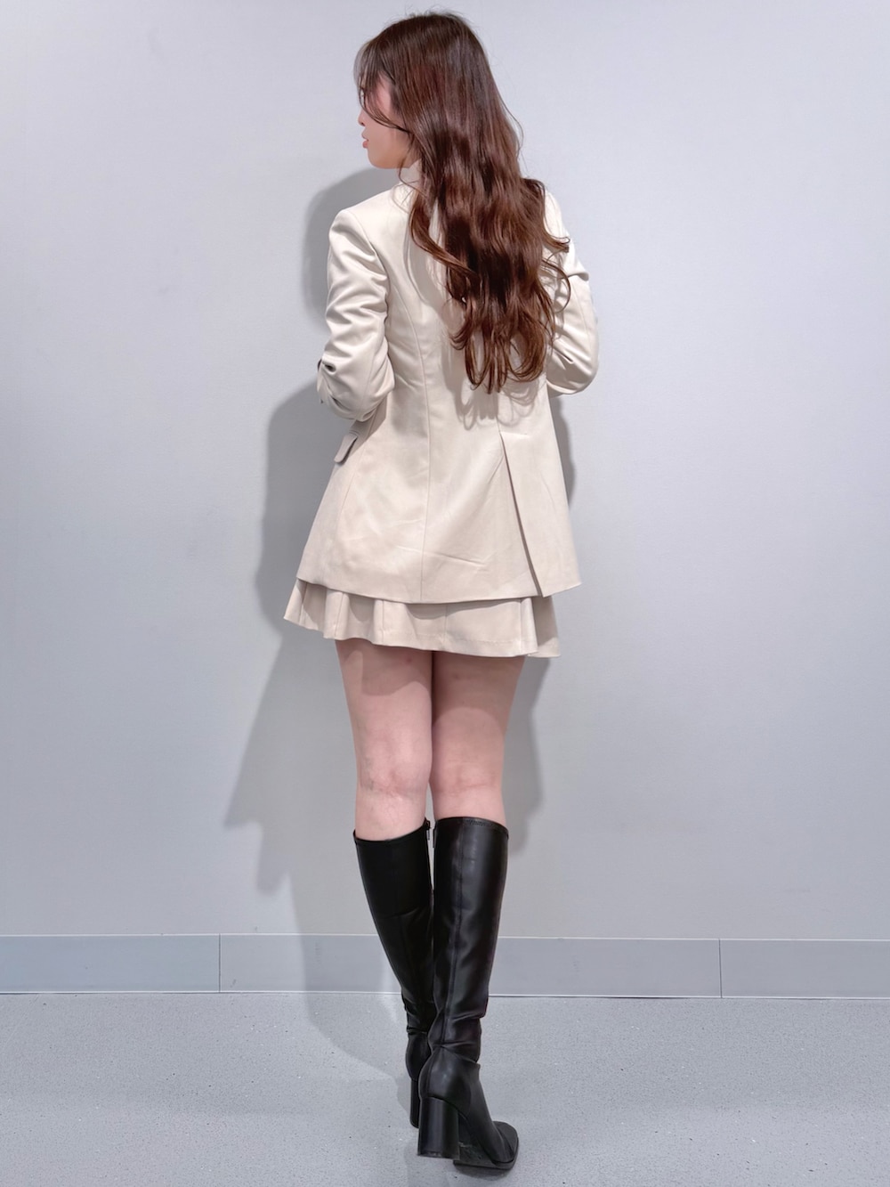ホワイト系のテーラードジャケット、ブラック系のブーツ、ホワイト系のスカートを着用したレディースの冬コーディネートの3枚目の写真
