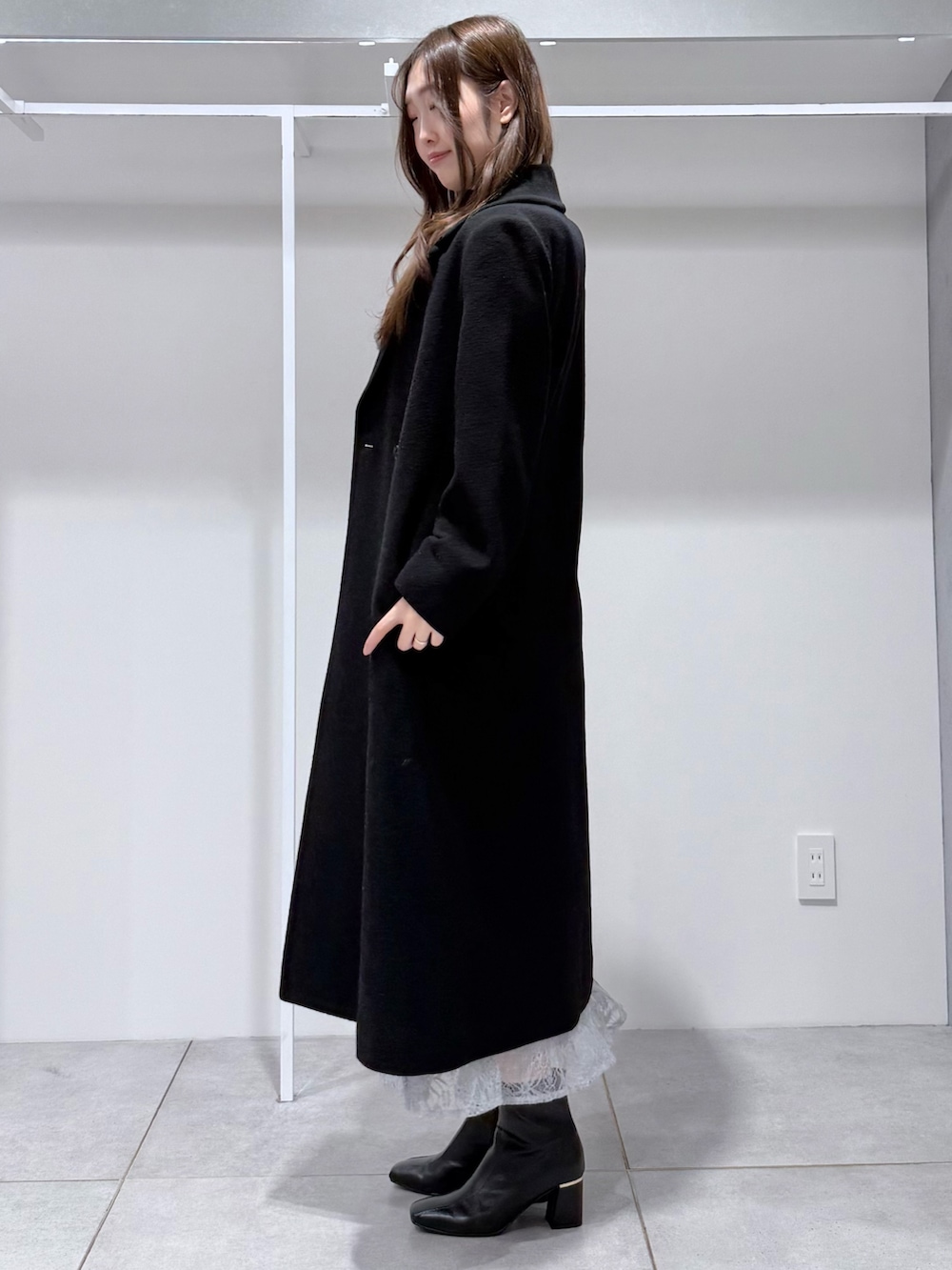 ブラック系のチェスターコート、ブラック系のニット/セーター、ブルー系のスカートを着用したレディースの冬コーディネートの3枚目の写真