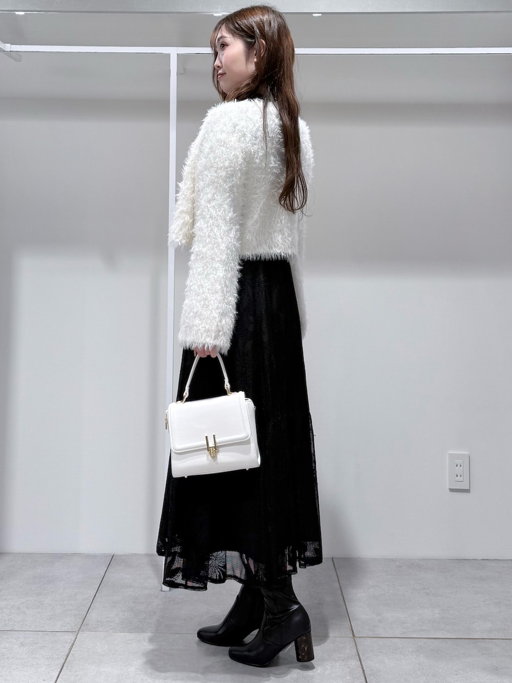 ブラック系のワンピース、ホワイト系のカーディガン/ボレロ、ホワイト系のハンドバッグを着用したレディースの冬コーディネートの4枚目の写真