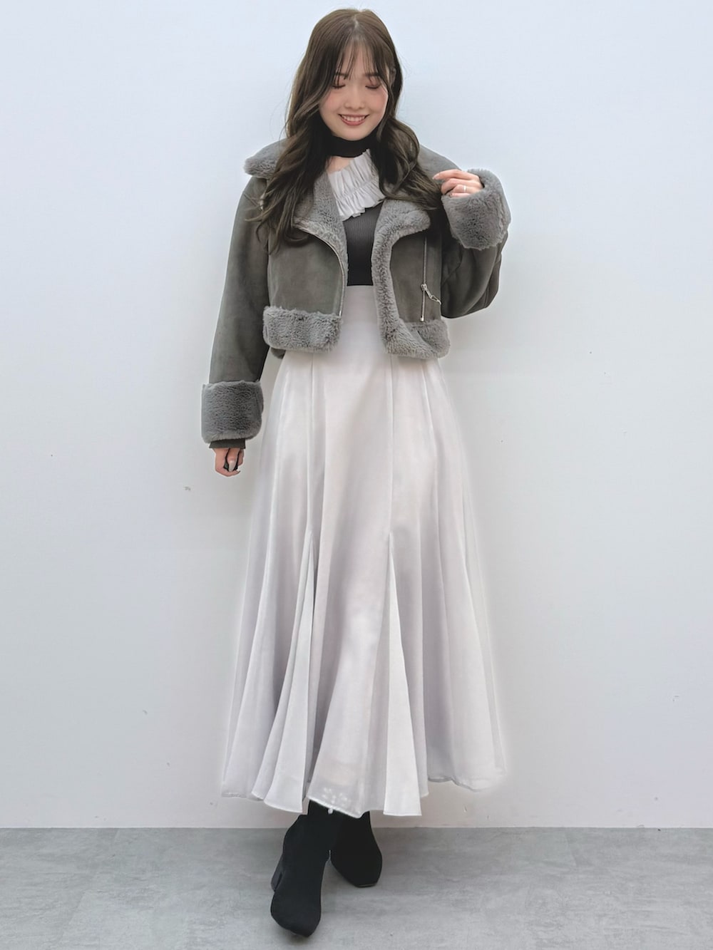 グレー系のスカート、ブラック系のブーツ、グレー系のムートンコートを着用したレディースの秋コーディネートの2枚目の写真