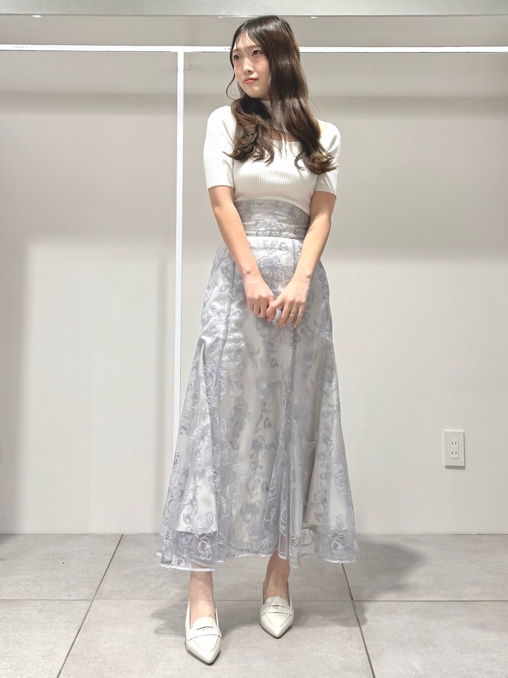 ホワイト系のニット/セーター、ブルー系のスカート、ホワイト系のパンプスを着用したレディースの春コーディネートの2枚目の写真