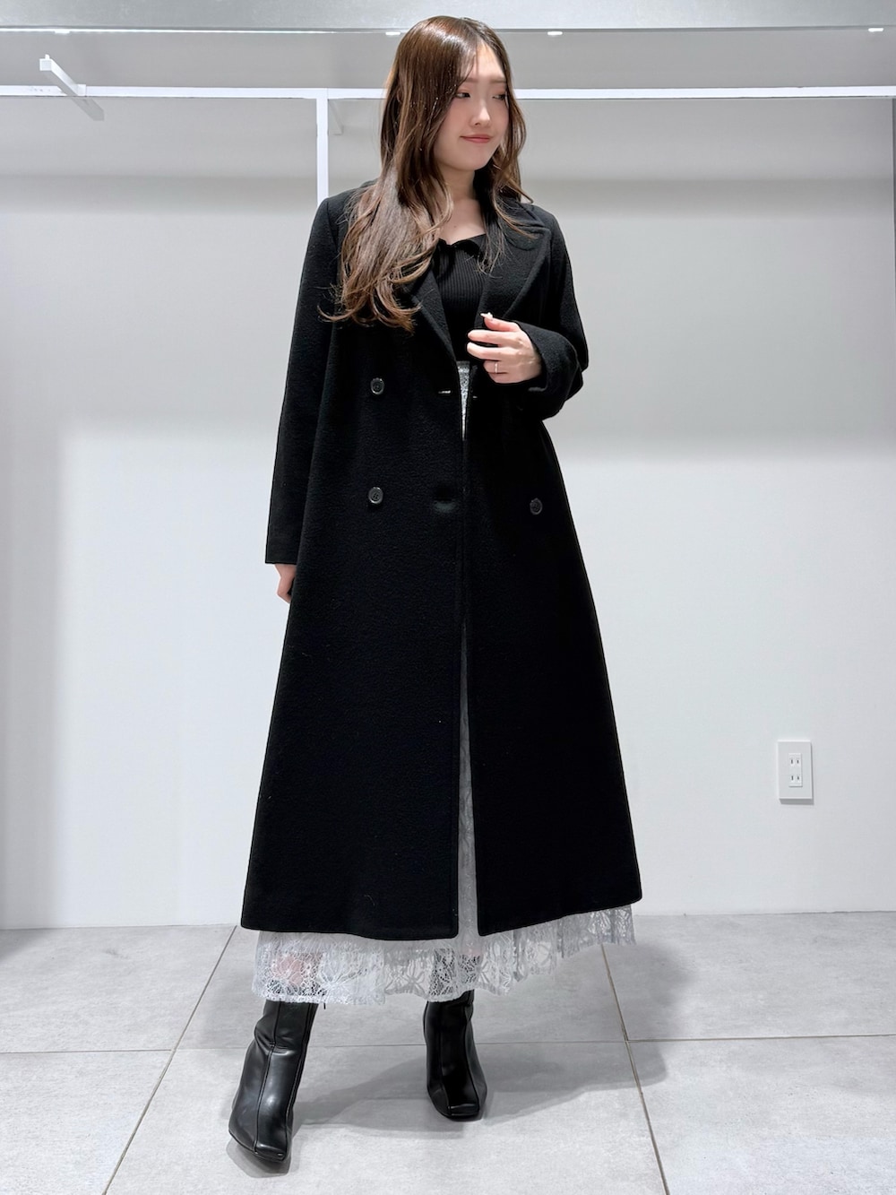 ブラック系のチェスターコート、ブラック系のニット/セーター、ブルー系のスカートを着用したレディースの冬コーディネートの2枚目の写真