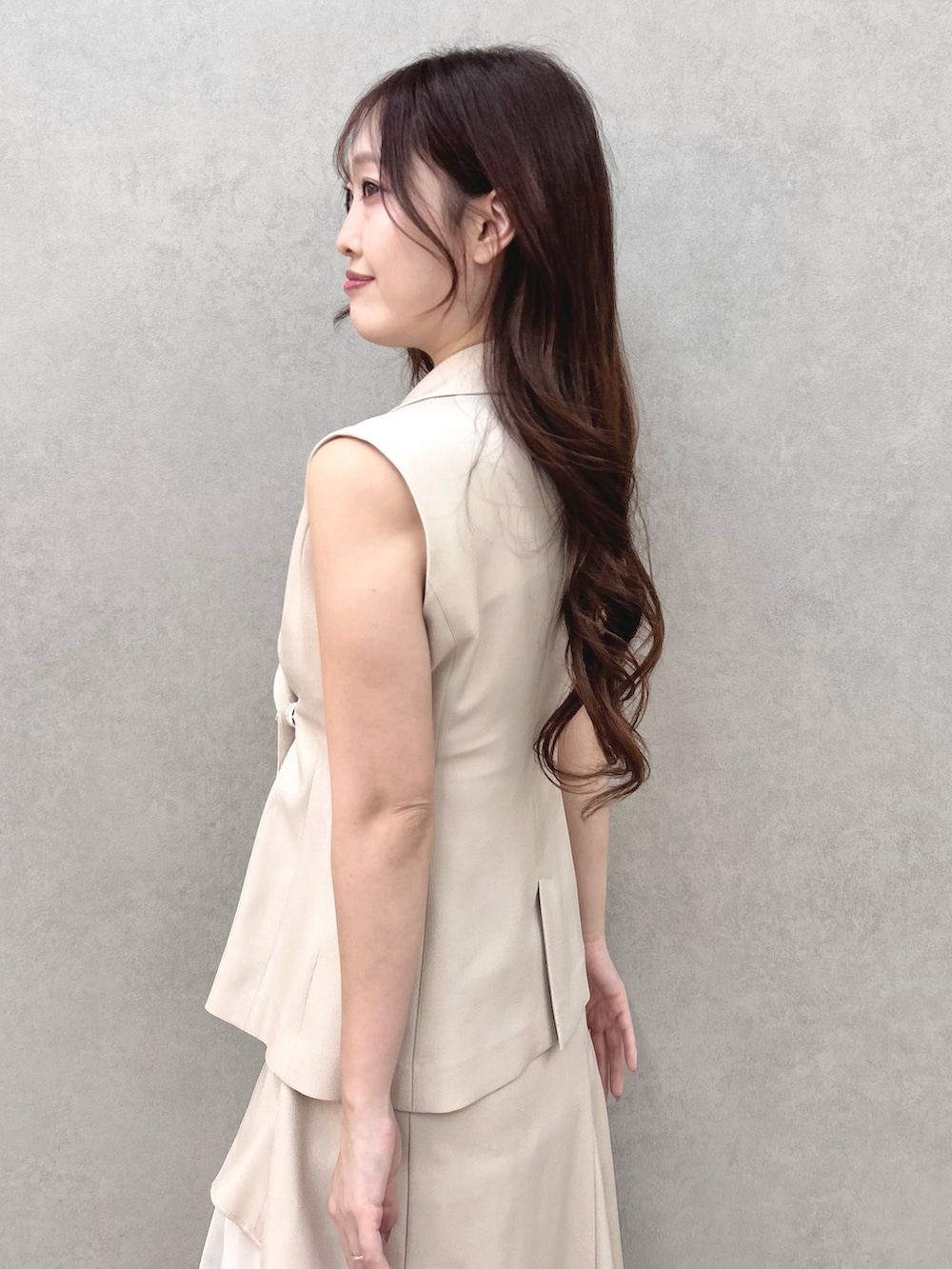 シルバー系のサンダル、ベージュ系のスカート、ベージュ系のベストを着用したレディースの春コーディネートの6枚目の写真