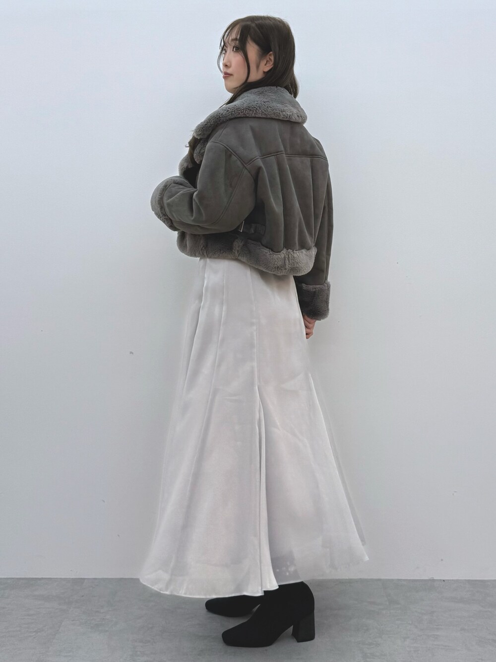 グレー系のスカート、ブラック系のブーツ、グレー系のムートンコートを着用したレディースの秋コーディネートの3枚目の写真