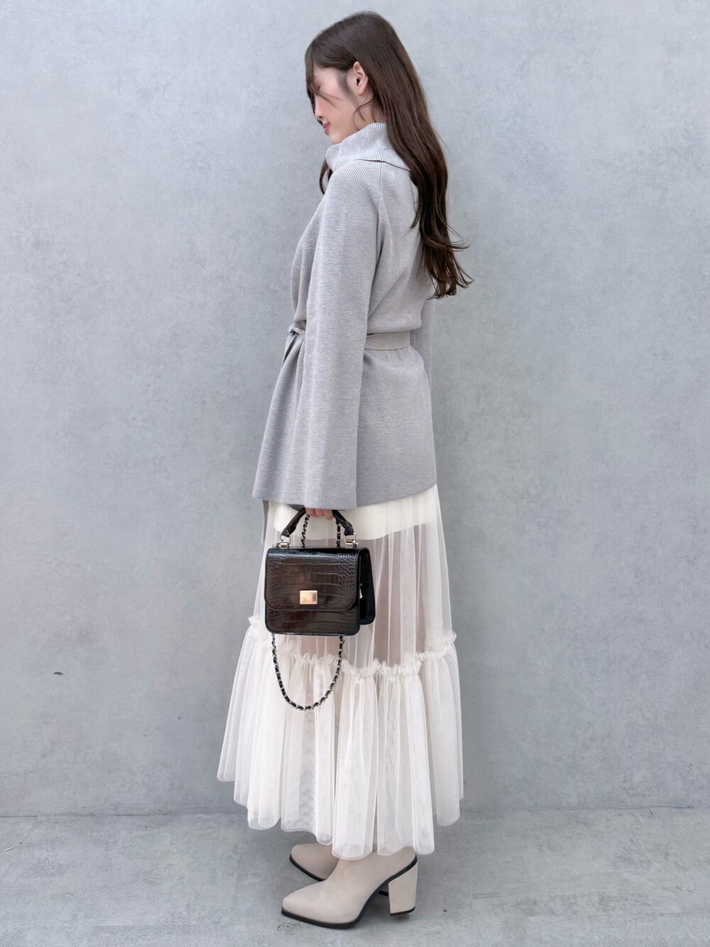 ブラック系のハンドバッグ、グレー系のニット/セーター、ホワイト系のスカートを着用したレディースの夏コーディネートの2枚目の写真