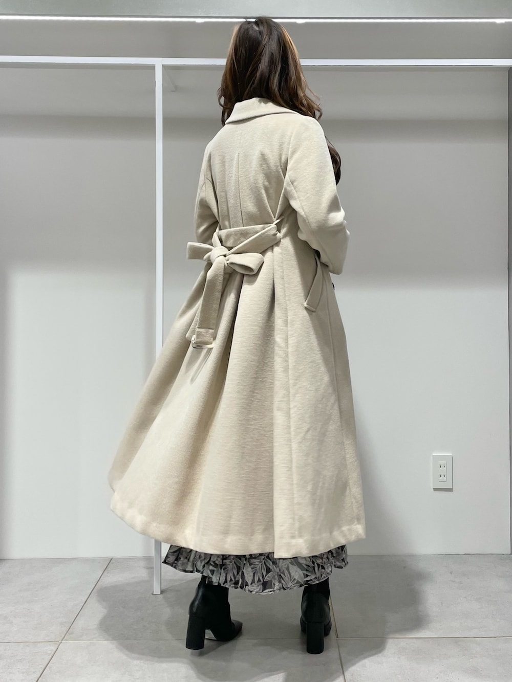 ベージュ系のチェスターコート、ブラック系のブーツ、ブラック系のスカートを着用したレディースの冬コーディネートの2枚目の写真