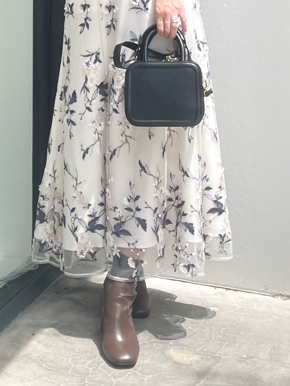 ブラック系のハンドバッグ、ブラウン系のブーツ、グレー系のスカートを着用したレディースの秋コーディネートの8枚目の写真