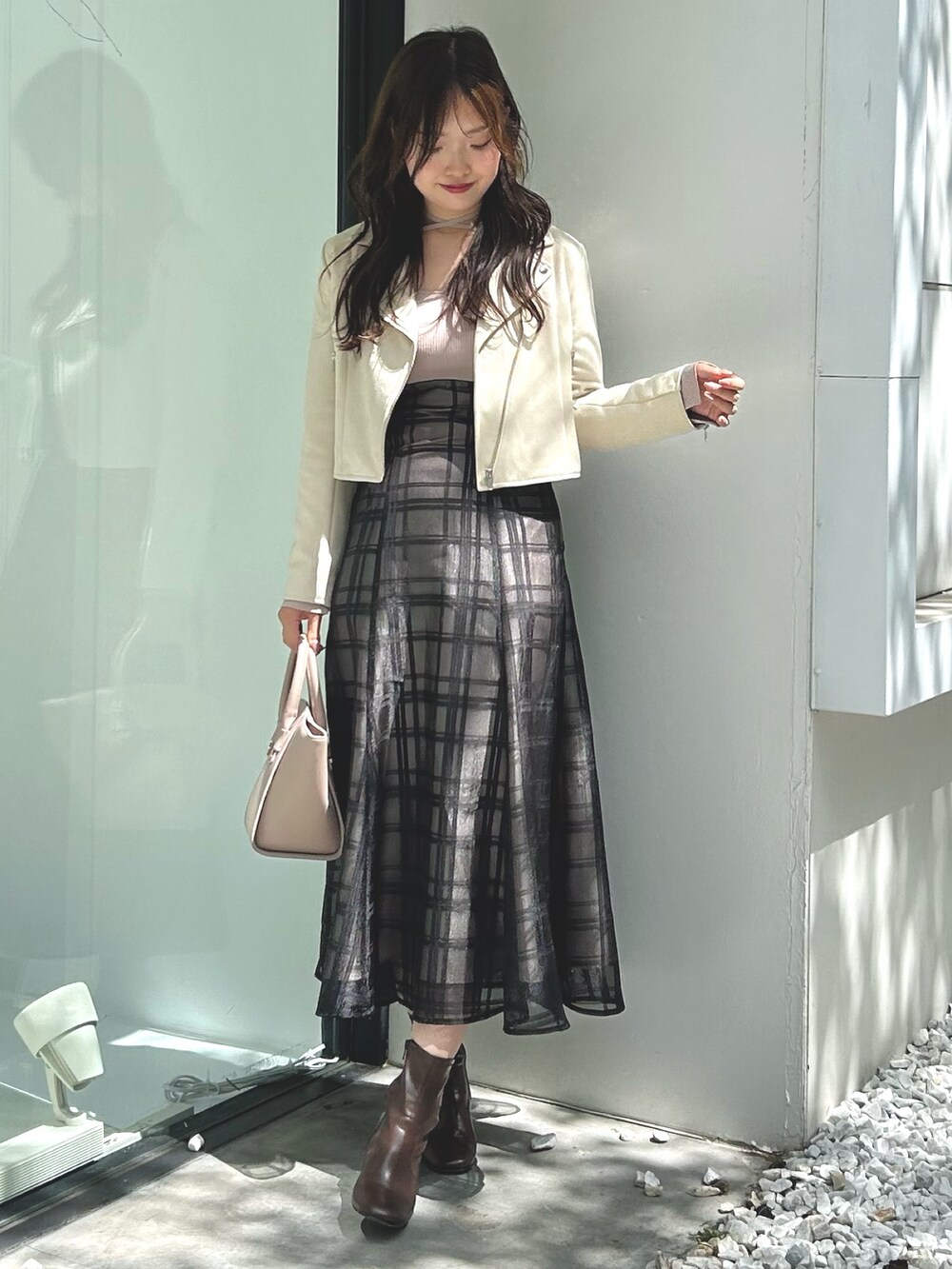 ピンク系のワンピース、ベージュ系のハンドバッグ、ホワイト系のライダースジャケットを着用したレディースの秋コーディネートの2枚目の写真