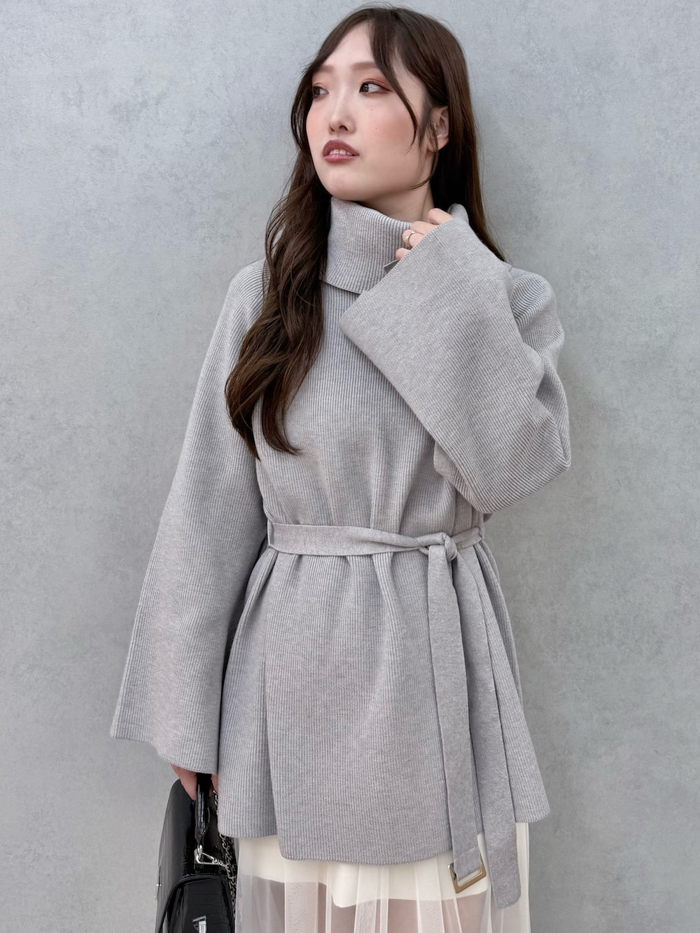 ブラック系のハンドバッグ、グレー系のニット/セーター、ホワイト系のスカートを着用したレディースの夏コーディネートの4枚目の写真