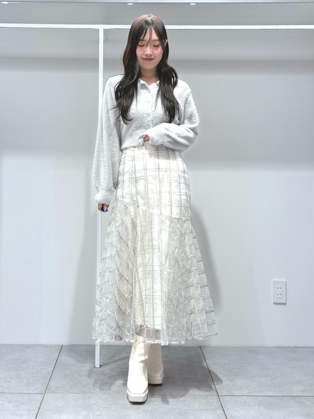 ブルー系のチェスターコート、ホワイト系のスカート、グレー系のカーディガン/ボレロを着用したレディースの秋コーディネートの7枚目の写真