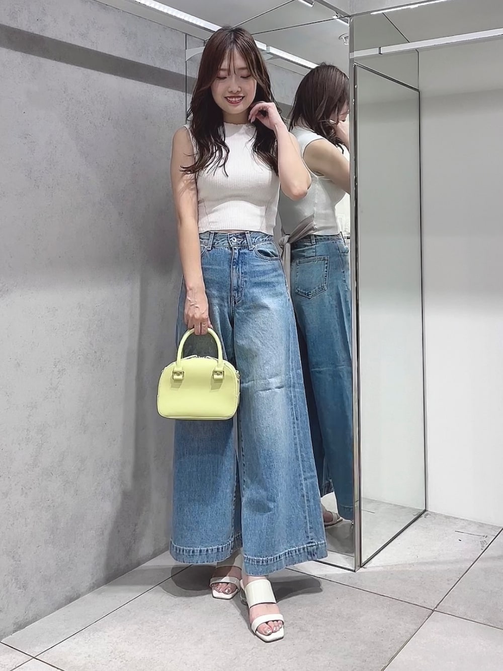 イエロー系のボストンバッグ、ブルー系のデニムパンツ、ホワイト系のニット/セーターを着用したレディースの夏コーディネートの2枚目の写真