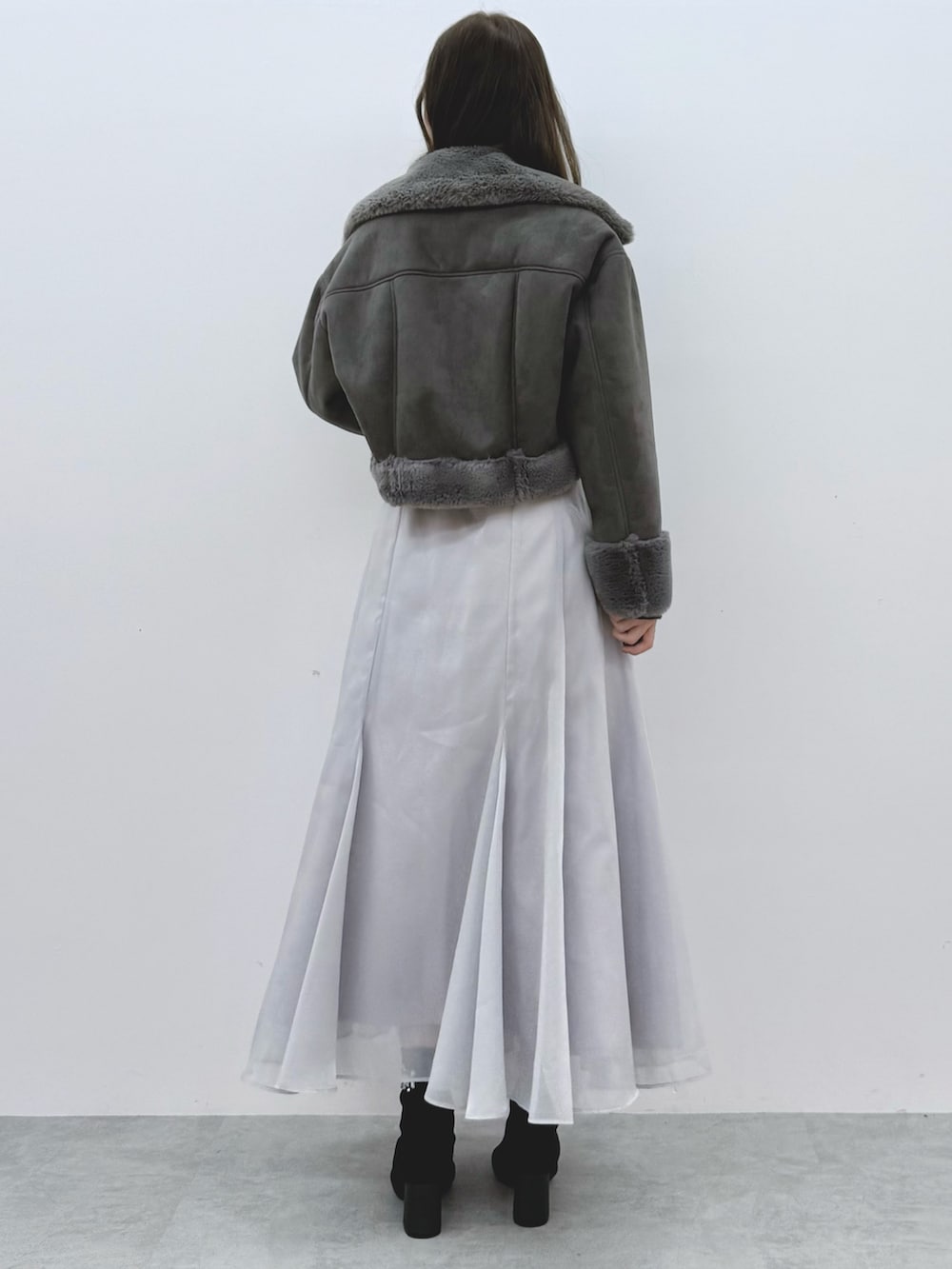 グレー系のスカート、ブラック系のブーツ、グレー系のムートンコートを着用したレディースの秋コーディネートの4枚目の写真