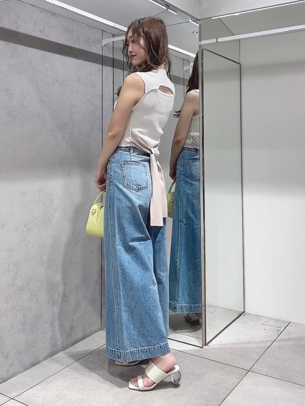 イエロー系のボストンバッグ、ブルー系のデニムパンツ、ホワイト系のニット/セーターを着用したレディースの夏コーディネートの3枚目の写真