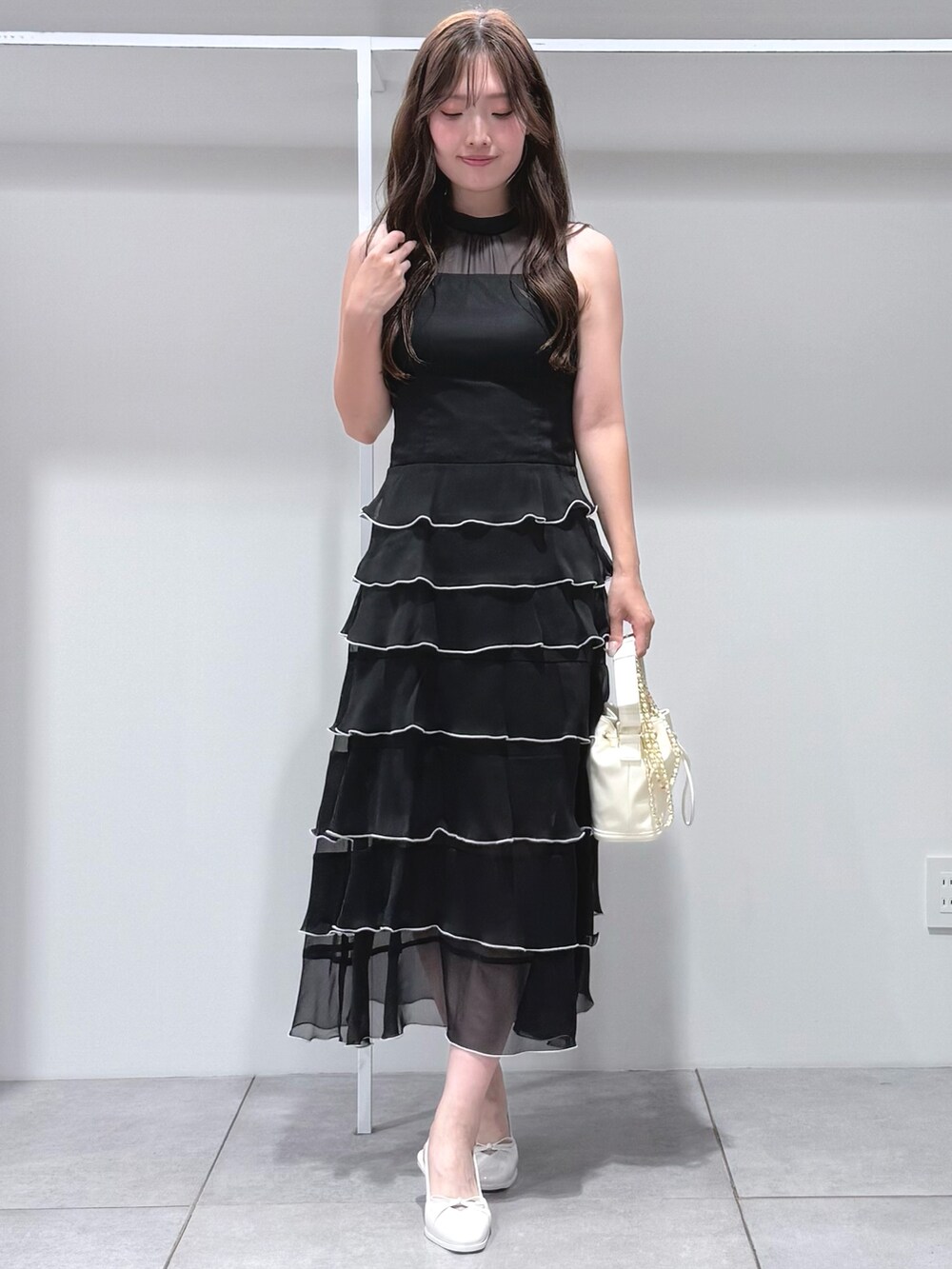 ホワイト系のハンドバッグ、ブラック系のワンピース、ホワイト系のパンプスを着用したレディースの夏コーディネートの2枚目の写真