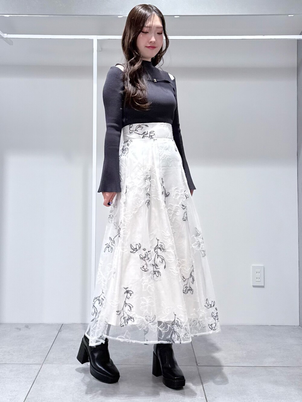 グレー系のニット/セーター、ブラック系のブーツ、ホワイト系のスカートを着用したレディースの冬コーディネートの2枚目の写真