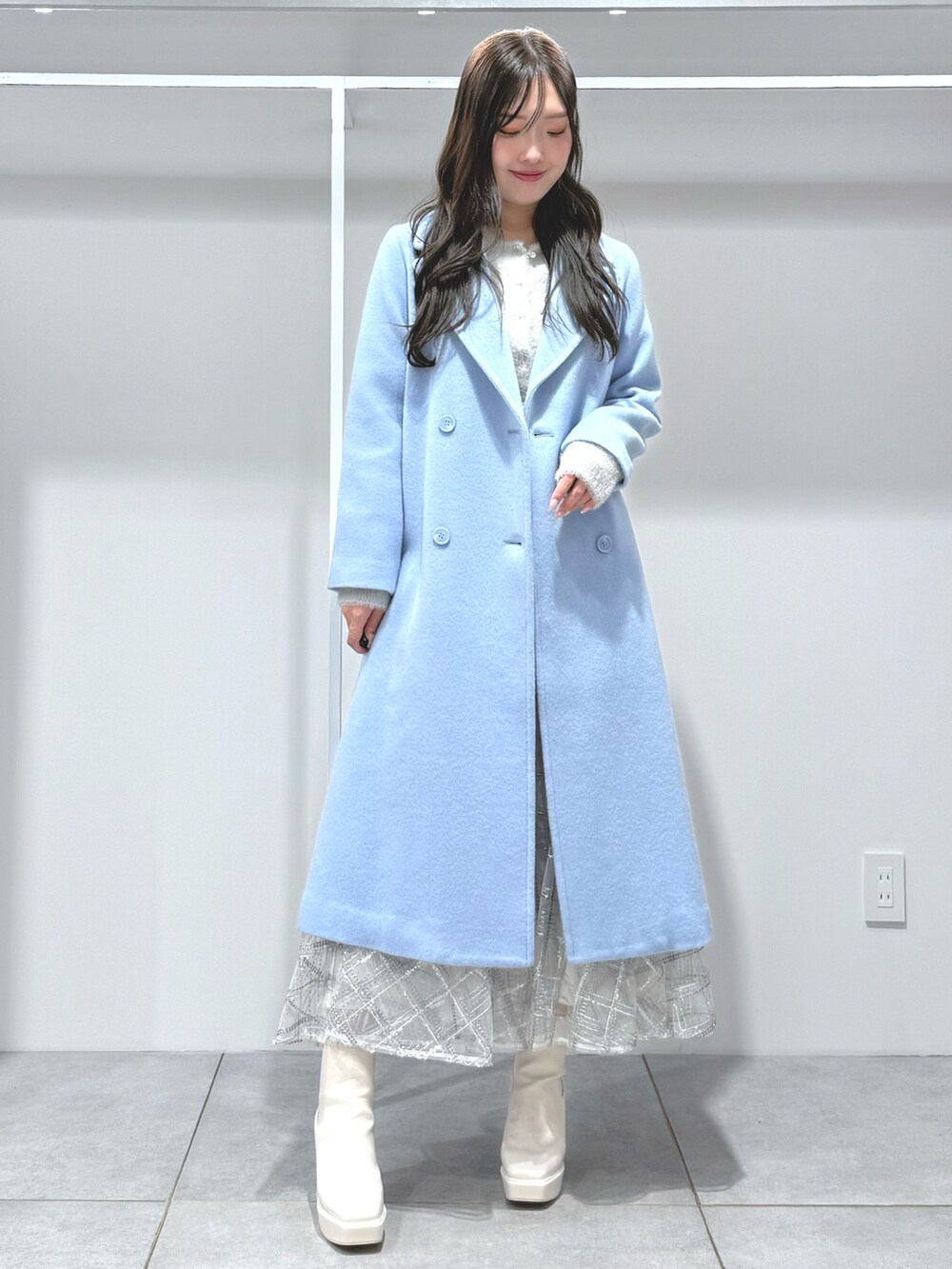 ブルー系のチェスターコート、ホワイト系のスカート、グレー系のカーディガン/ボレロを着用したレディースの秋コーディネートの2枚目の写真