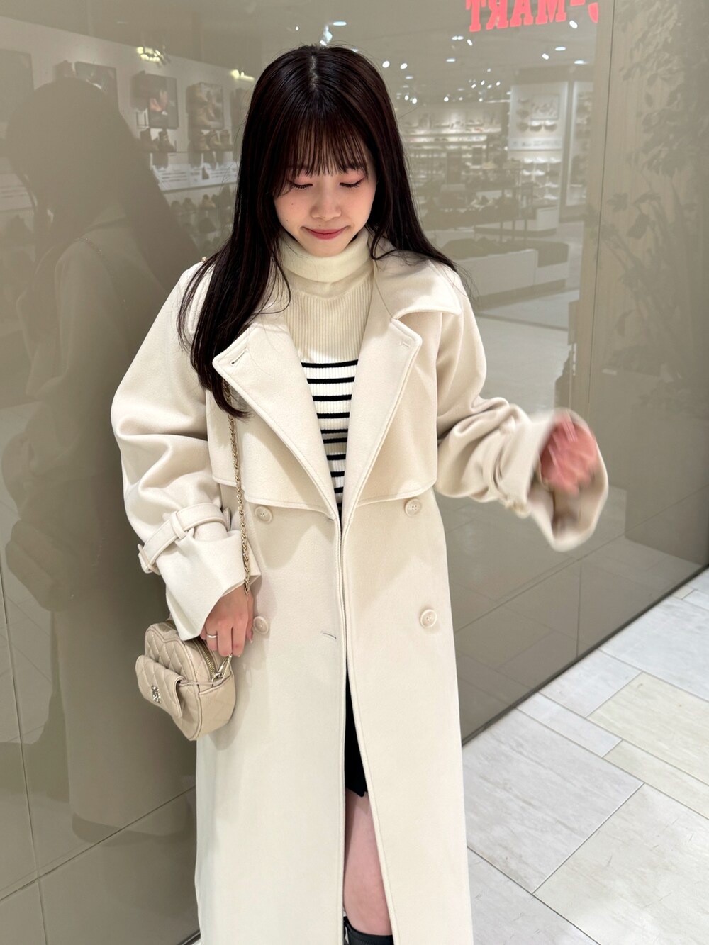 ホワイト系のステンカラーコート、ベージュ系のショルダーバッグ、ホワイト系のニット/セーターを着用したレディースの冬コーディネートの5枚目の写真