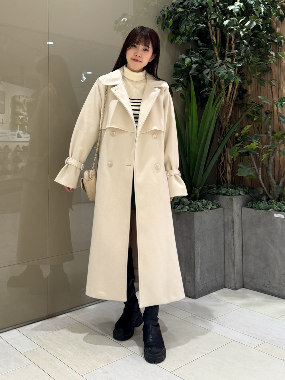 ホワイト系のステンカラーコート、ベージュ系のショルダーバッグ、ホワイト系のニット/セーターを着用したレディースの冬コーディネートの3枚目の写真