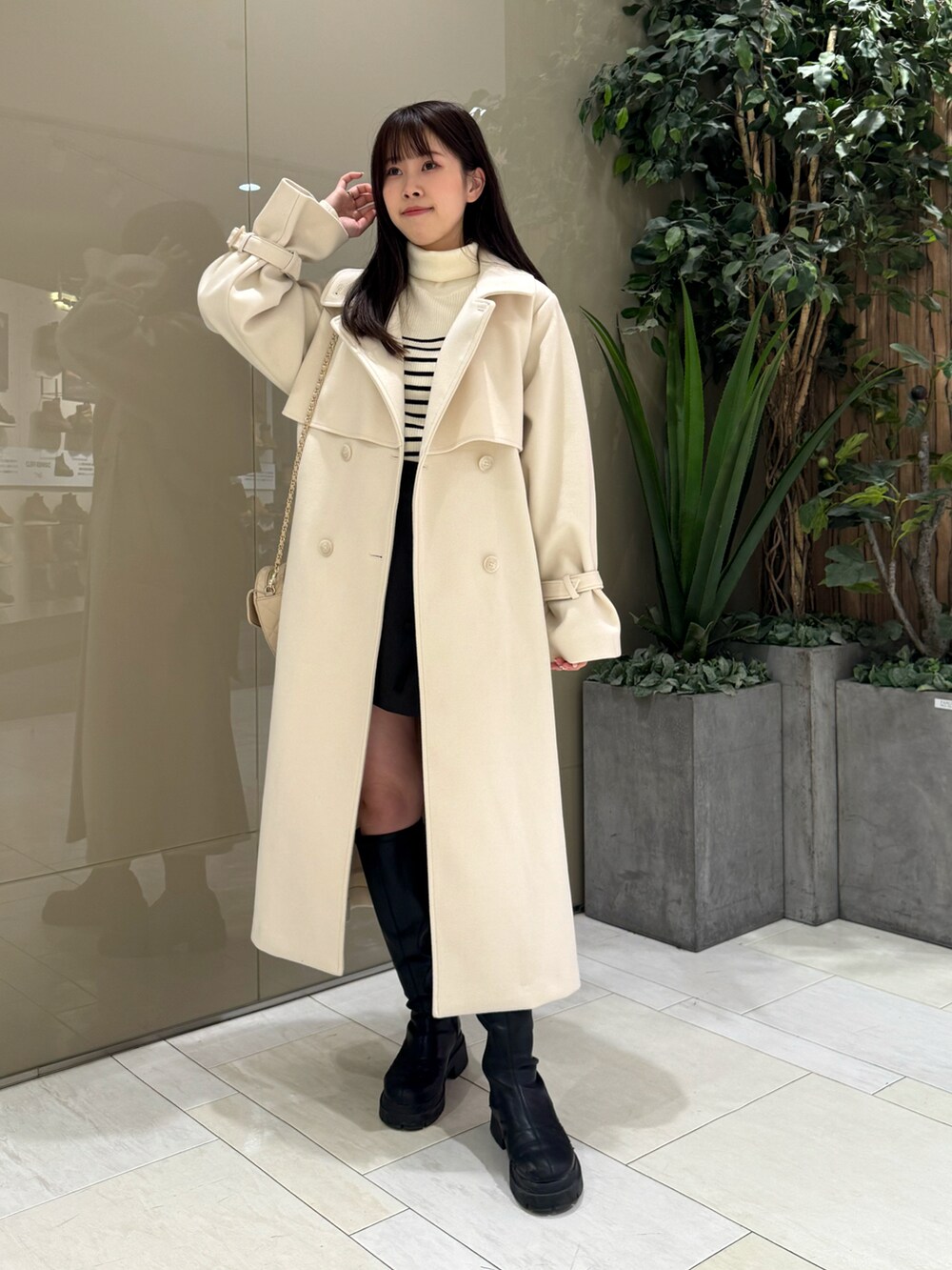 ホワイト系のステンカラーコート、ベージュ系のショルダーバッグ、ホワイト系のニット/セーターを着用したレディースの冬コーディネートの2枚目の写真