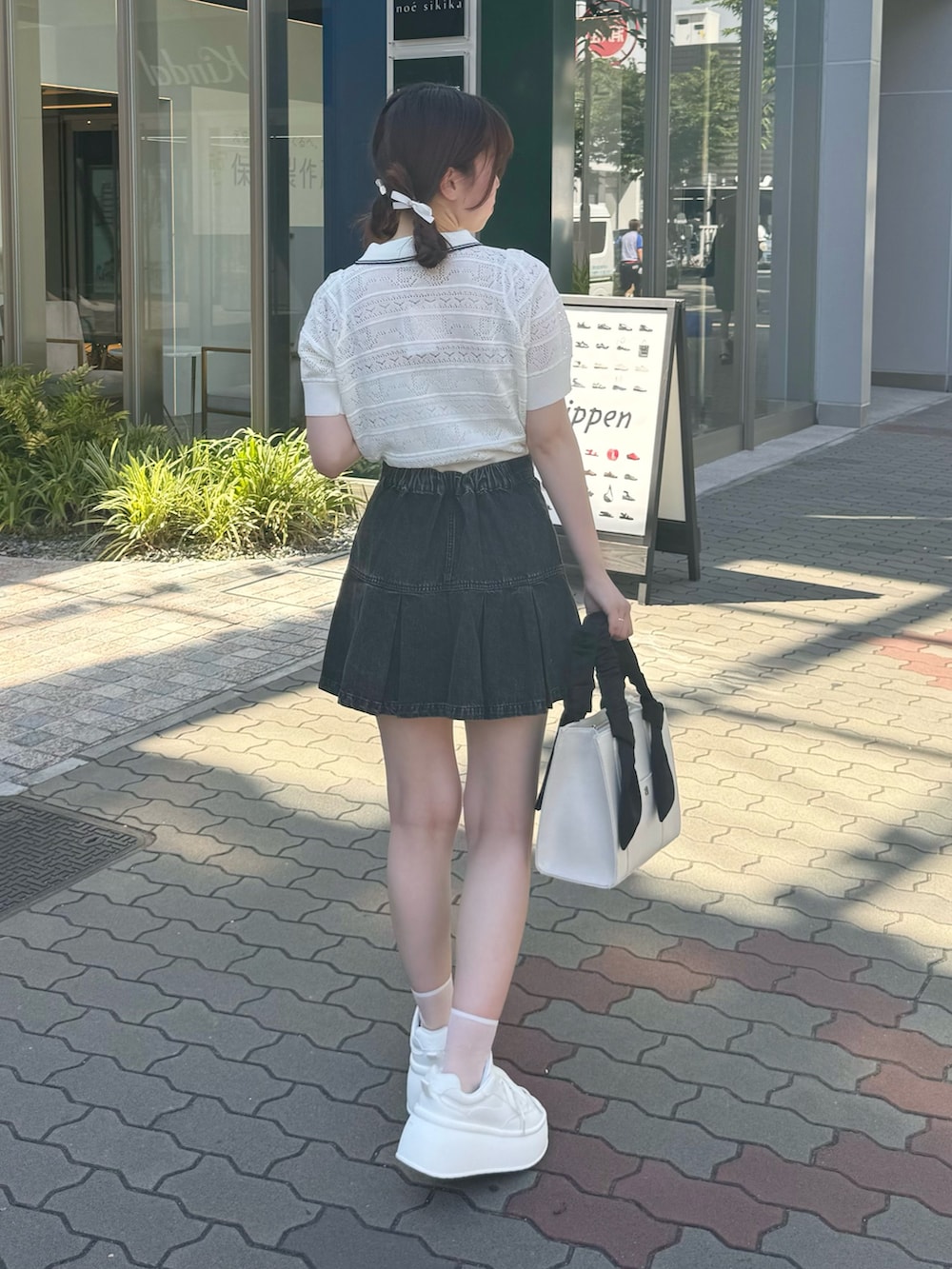 ホワイト系のニット/セーター、ブラック系のスカート、ホワイト系のスニーカーを着用したレディースの夏コーディネートの3枚目の写真