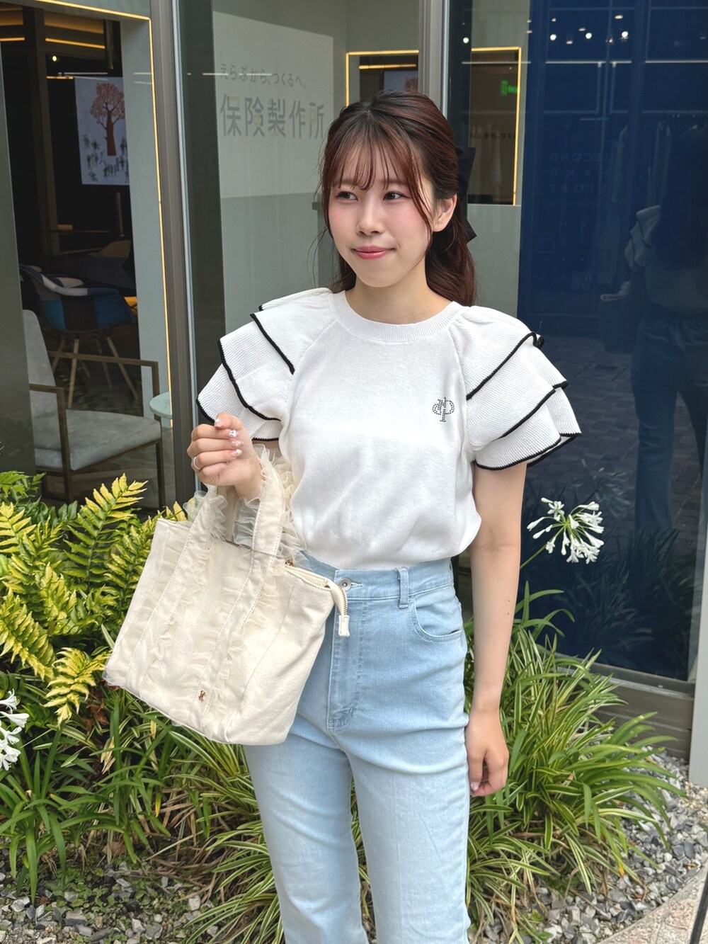 ホワイト系のニット/セーター、ホワイト系のトートバッグ、ブルー系のデニムパンツを着用したレディースの夏コーディネートの5枚目の写真