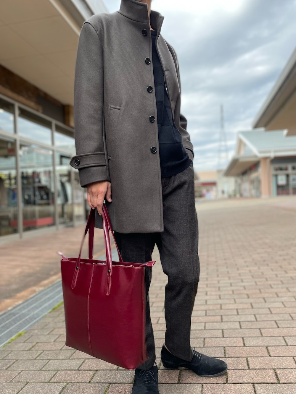 グレー系のチェスターコート、ブラック系のニット/セーター、ブラウン系のスラックスを着用したメンズの秋コーディネートの2枚目の写真