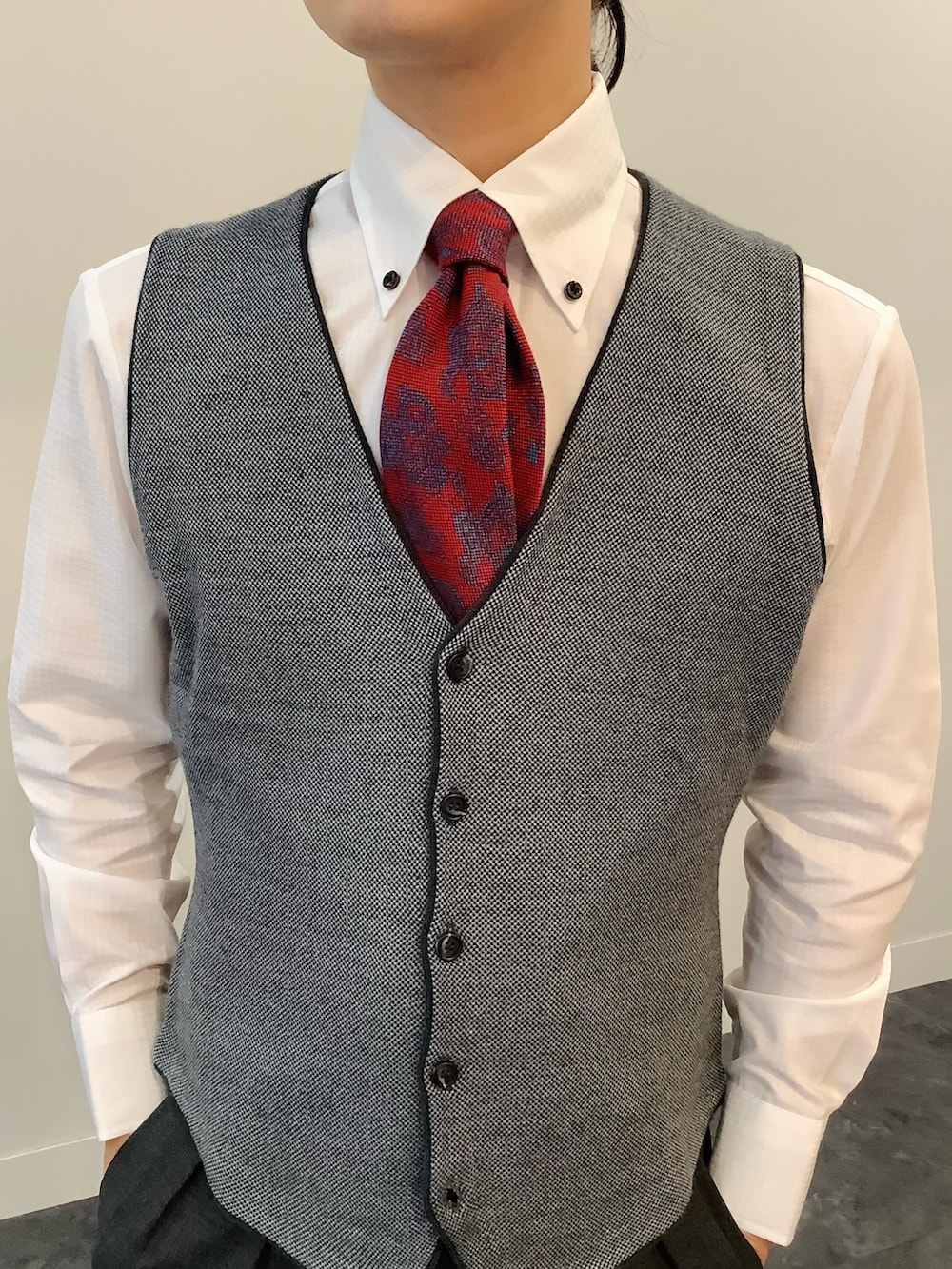 グレー系のベスト、ホワイト系のビジネスシャツ、レッド系のネクタイを着用したメンズの秋コーディネートの2枚目の写真