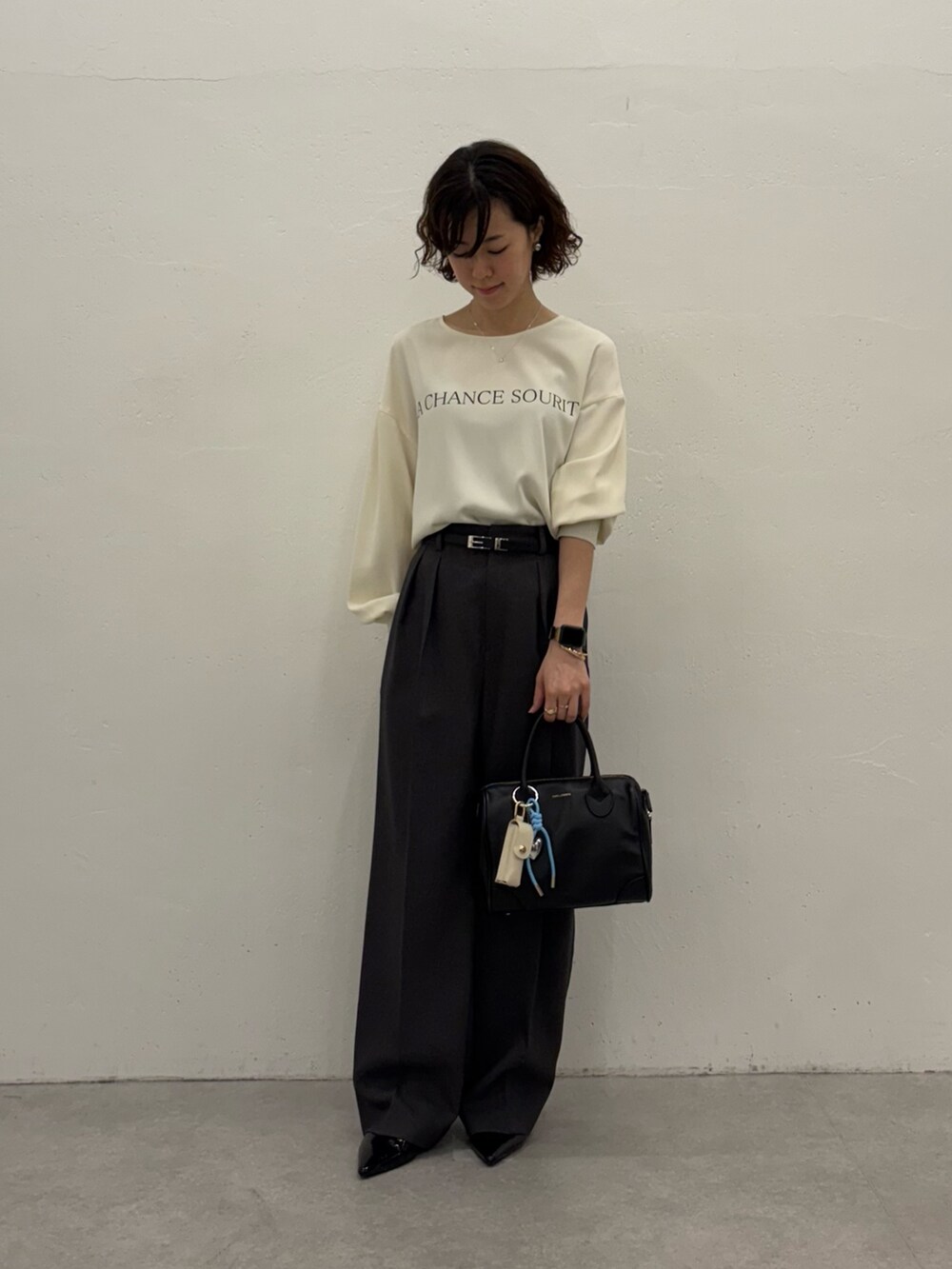 グレー系のスラックス、ホワイト系のTシャツ/カットソー、ブラック系のボストンバッグを着用したレディースの秋コーディネートの2枚目の写真