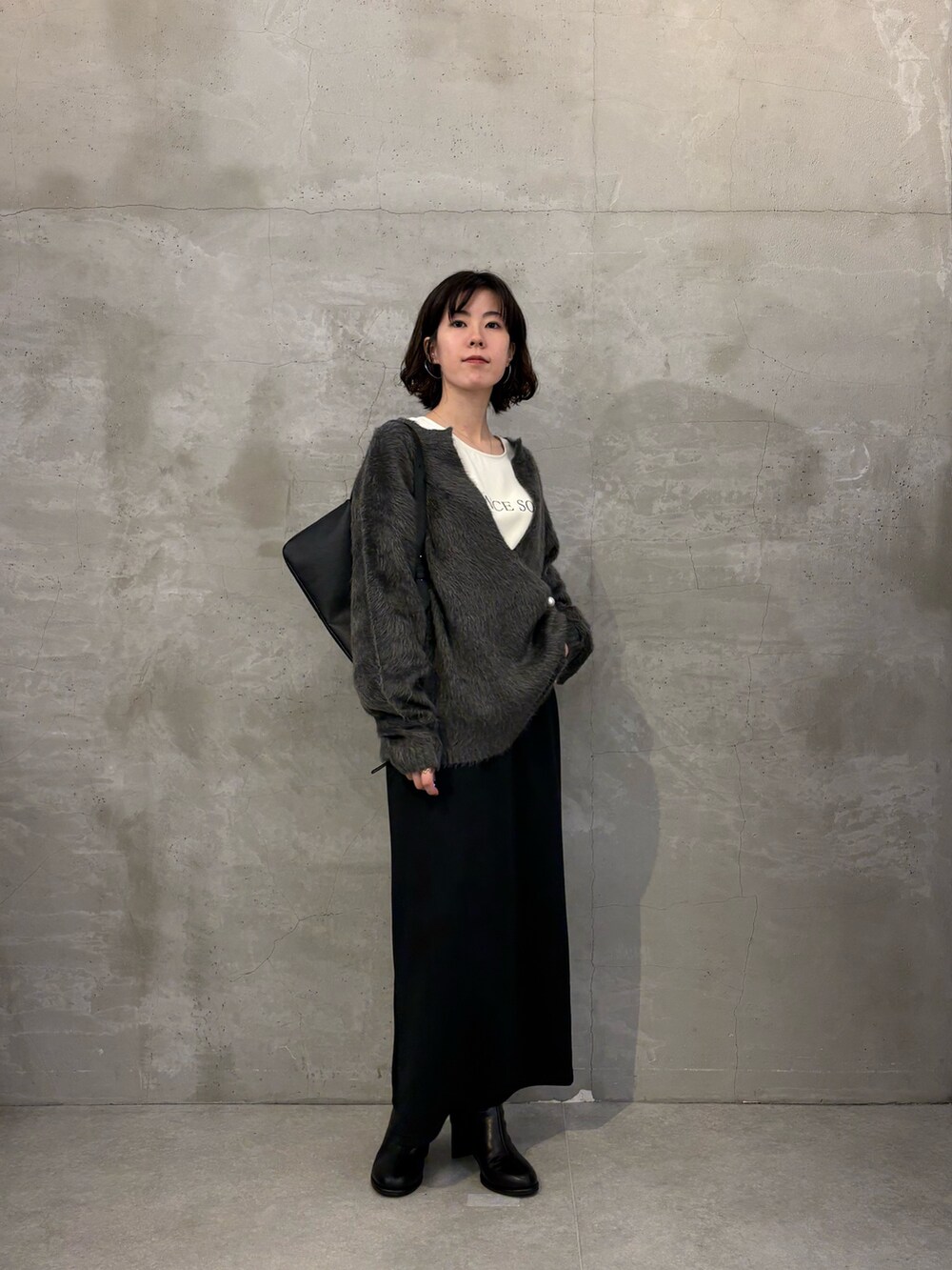 グレー系のニット/セーター、ブラック系のスカート、ホワイト系のTシャツ/カットソーを着用したレディースの秋コーディネートの4枚目の写真